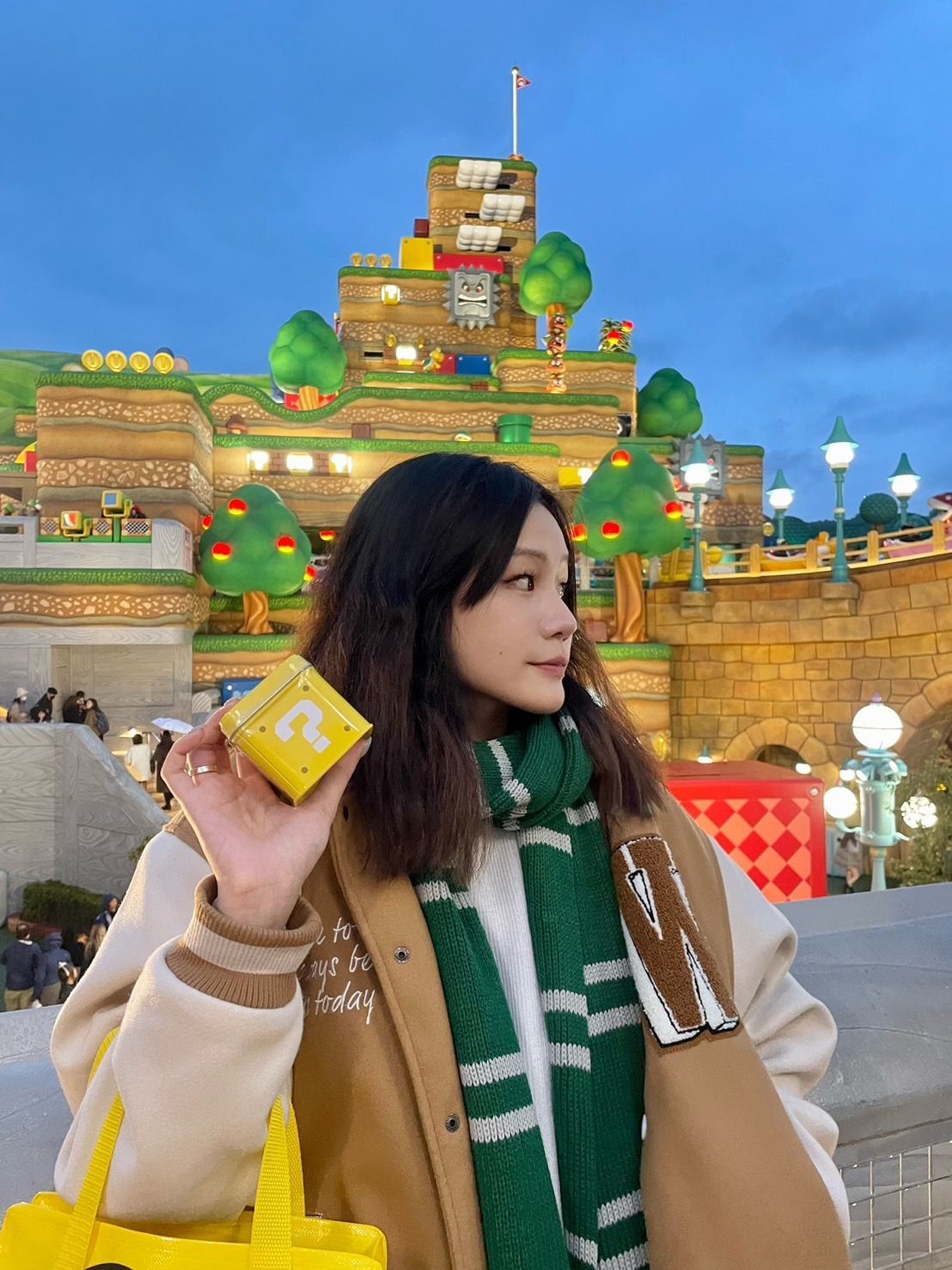 一位穿著棕色夾克和綠色圍巾的女性,手裡拿著一個印有問號的黃色盒子