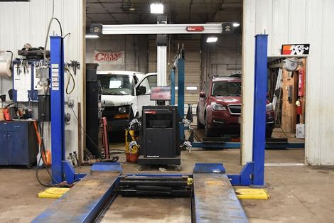 A car lift in an auto repair shop with a red SUV partially raised | Shawn's Auto Repair and Performance
