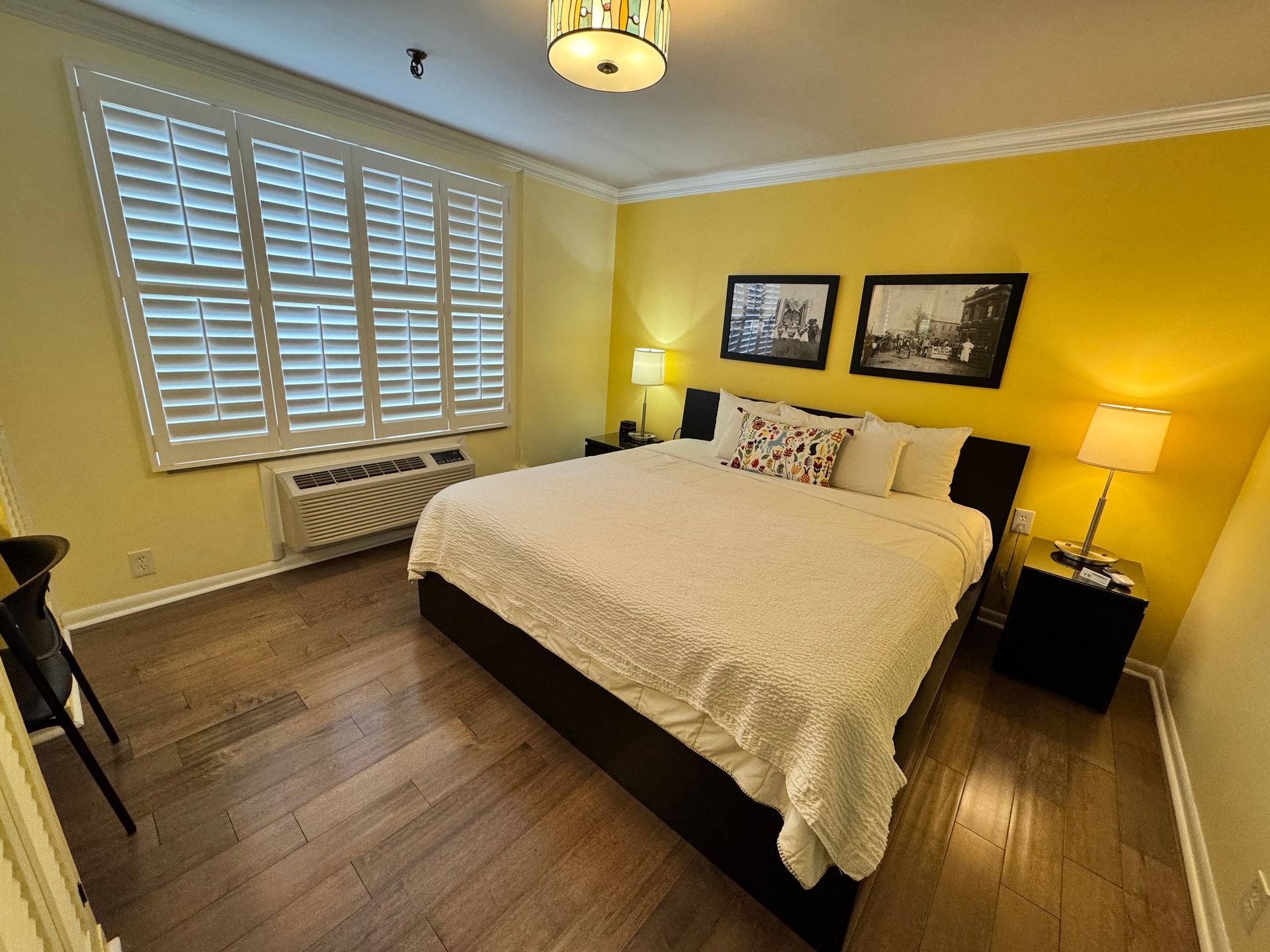 A bedroom with a king size bed , shutters on the windows and a desk.