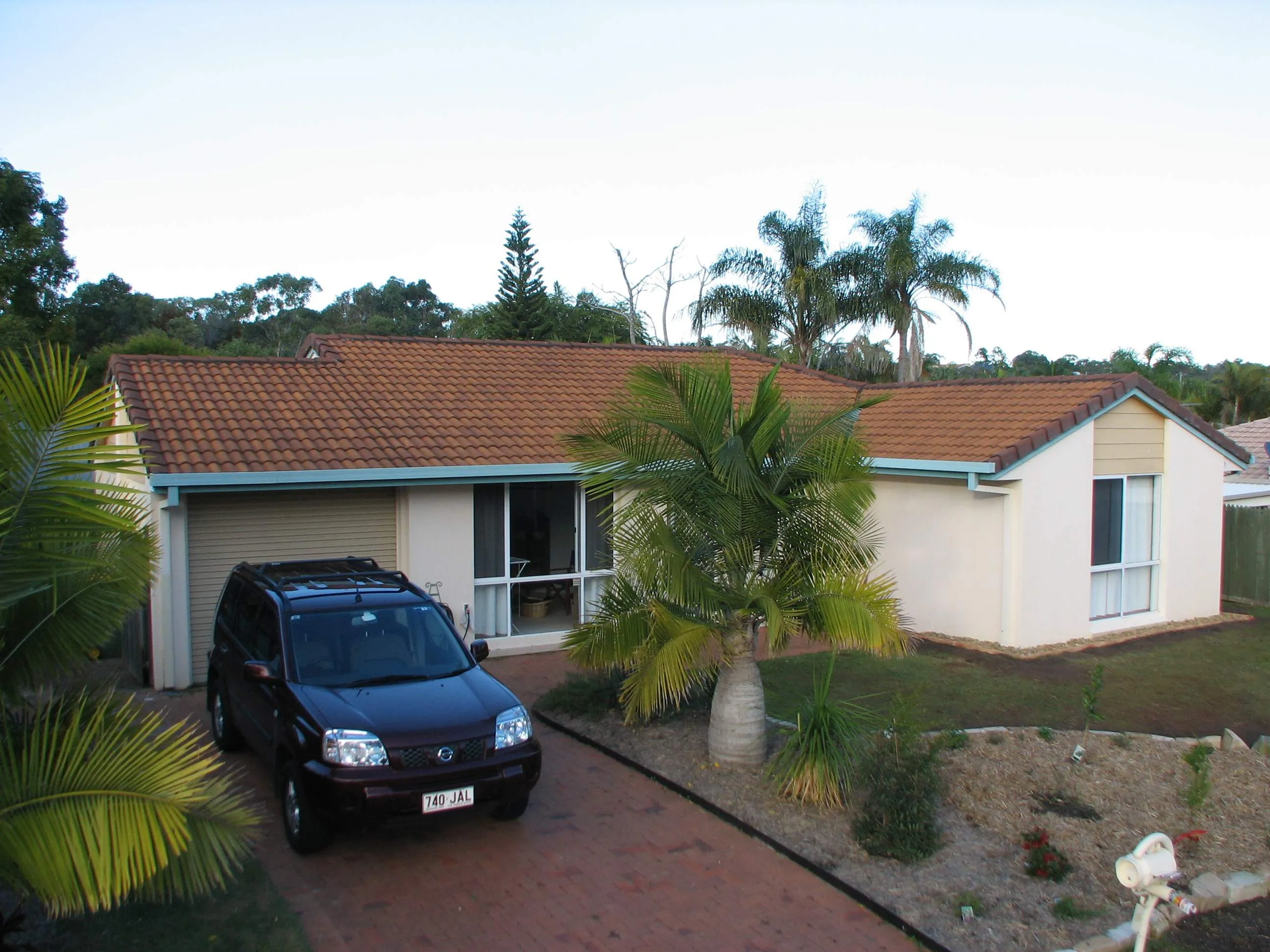 A car is parked in front of a house with a red tile roof