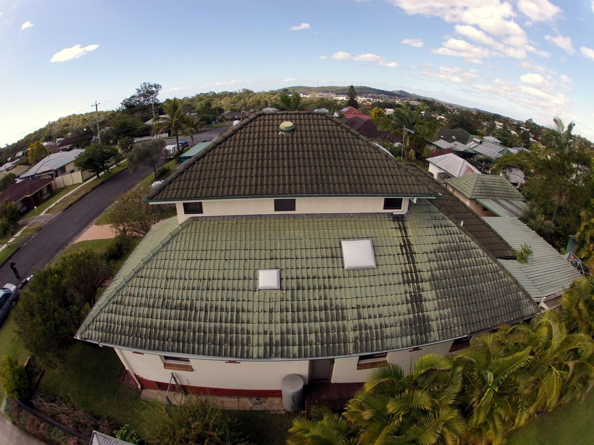 Aerial view of a large tiled roof with visible stains, discoloration, and signs of weather-related wear.