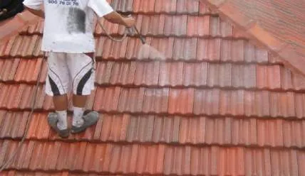 A man is cleaning a tiled roof with a pressure washer.