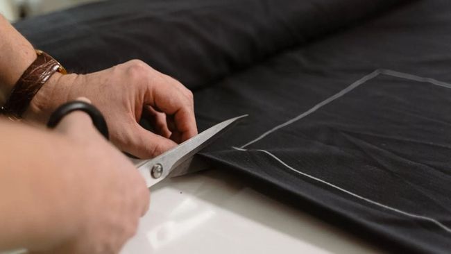 Manos cortando tela negra con tijeras sobre una superficie de trabajo.
