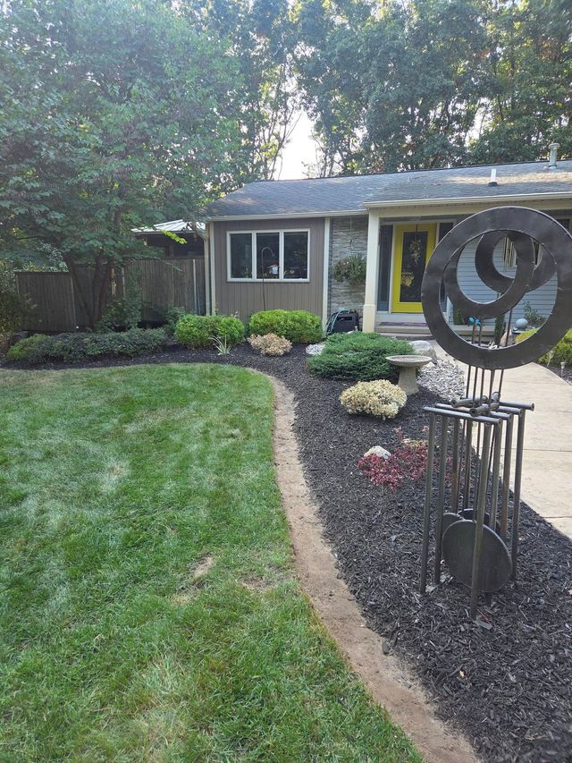 A house with a yellow door, landscaped garden beds, and lawn; decorative metal sculpture in the yard.