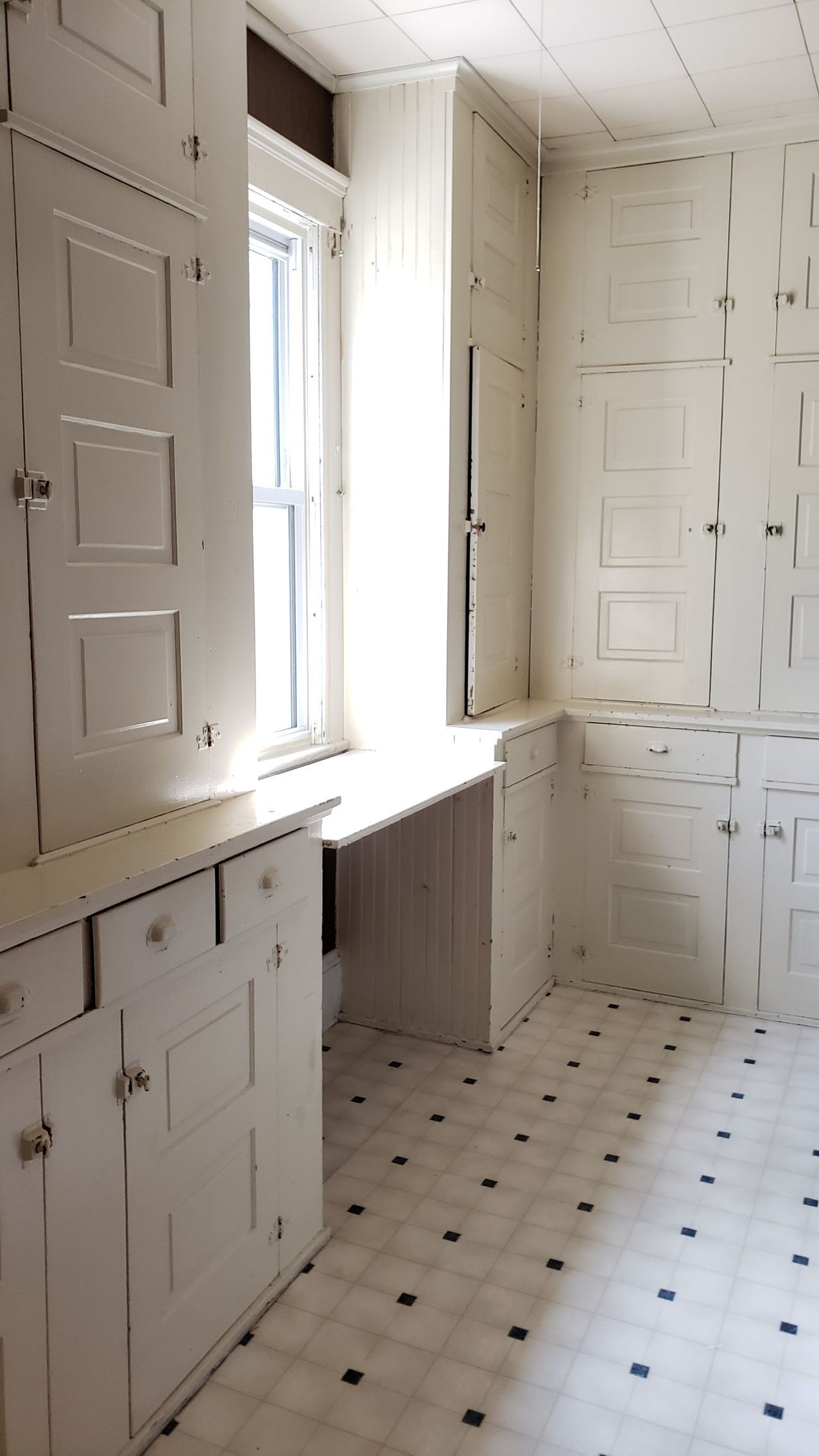 Bright white kitchen with paneled cabinets, tiled floor, and a window over a radiator.
