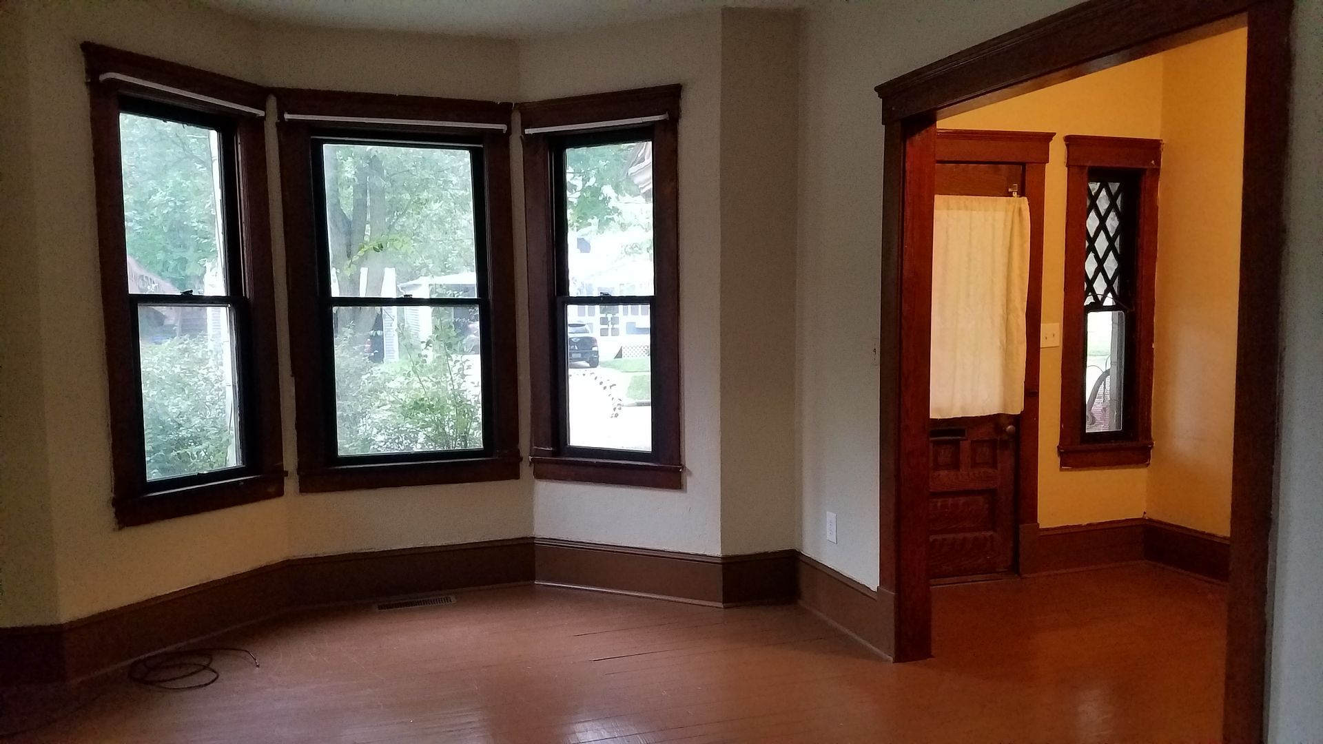 Empty room with bay windows, dark wood trim, and an open doorway to a warmly lit adjoining room
