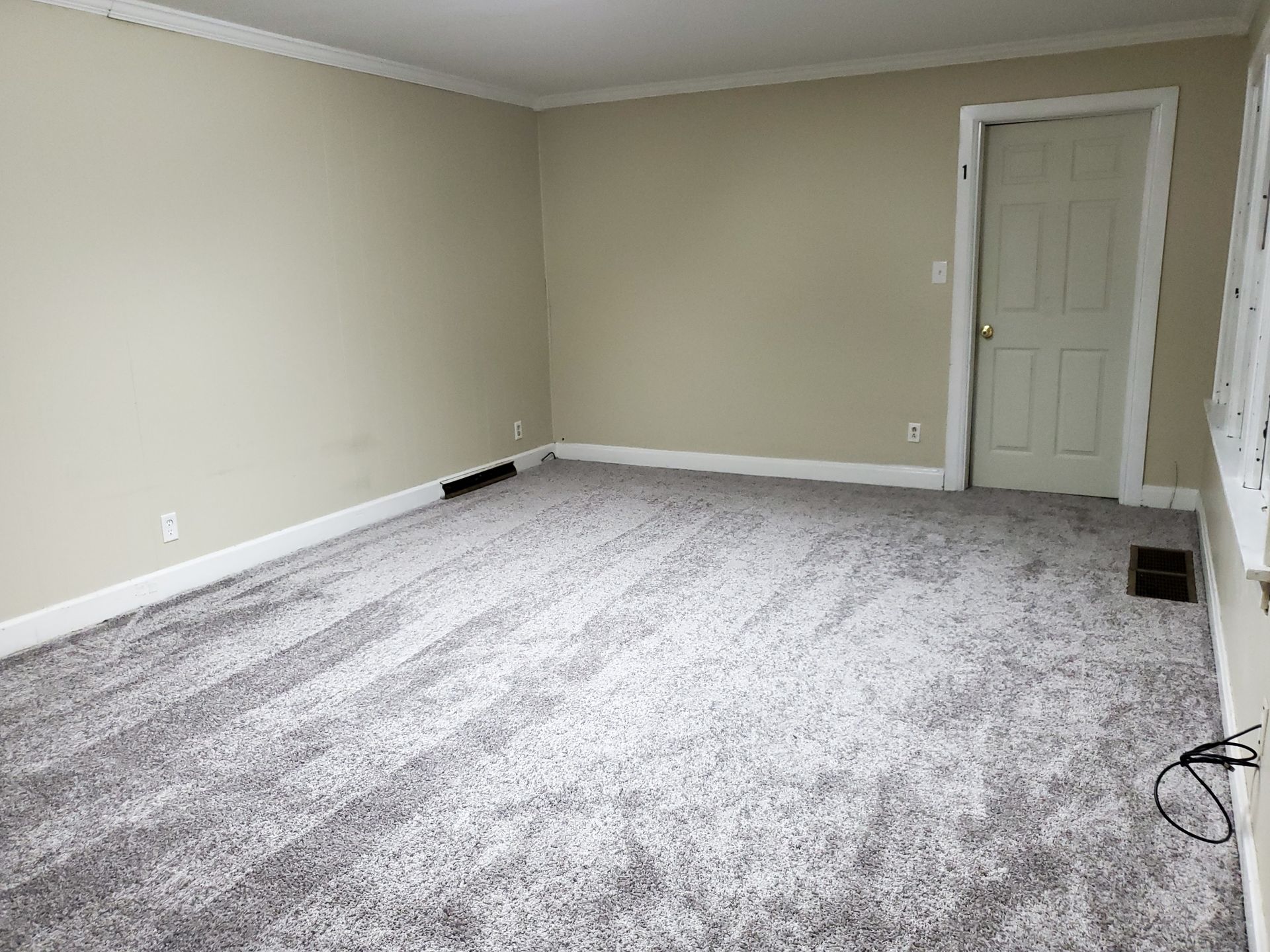 Empty beige room with gray carpet, closed door, and visible electrical outlets.