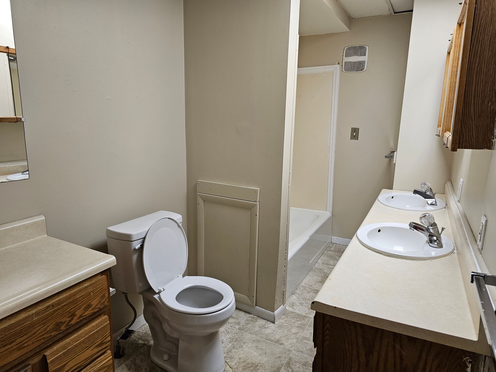 Small beige public restroom with toilet, sinks, and stall partitions