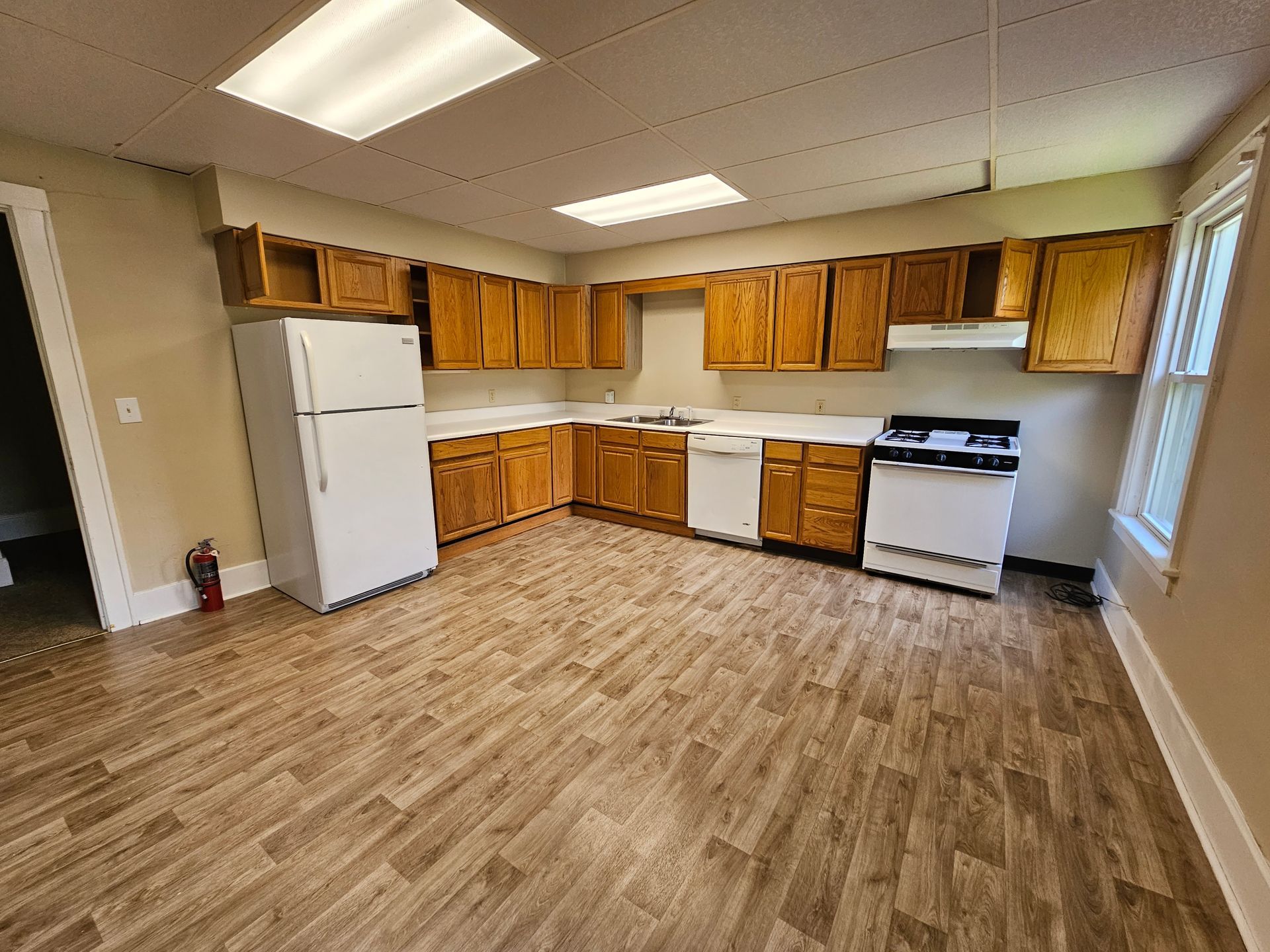 Empty kitchen with wooden cabinets, white appliances, and wood-look flooring under bright ceiling lights