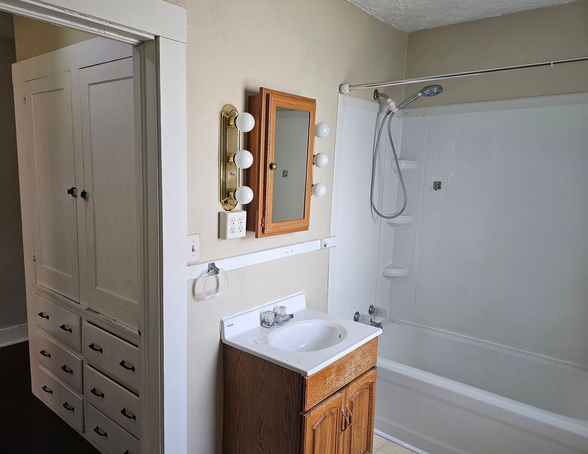 Bathroom with vanity, mirror lights, closet, and bathtub-shower in a small bright room