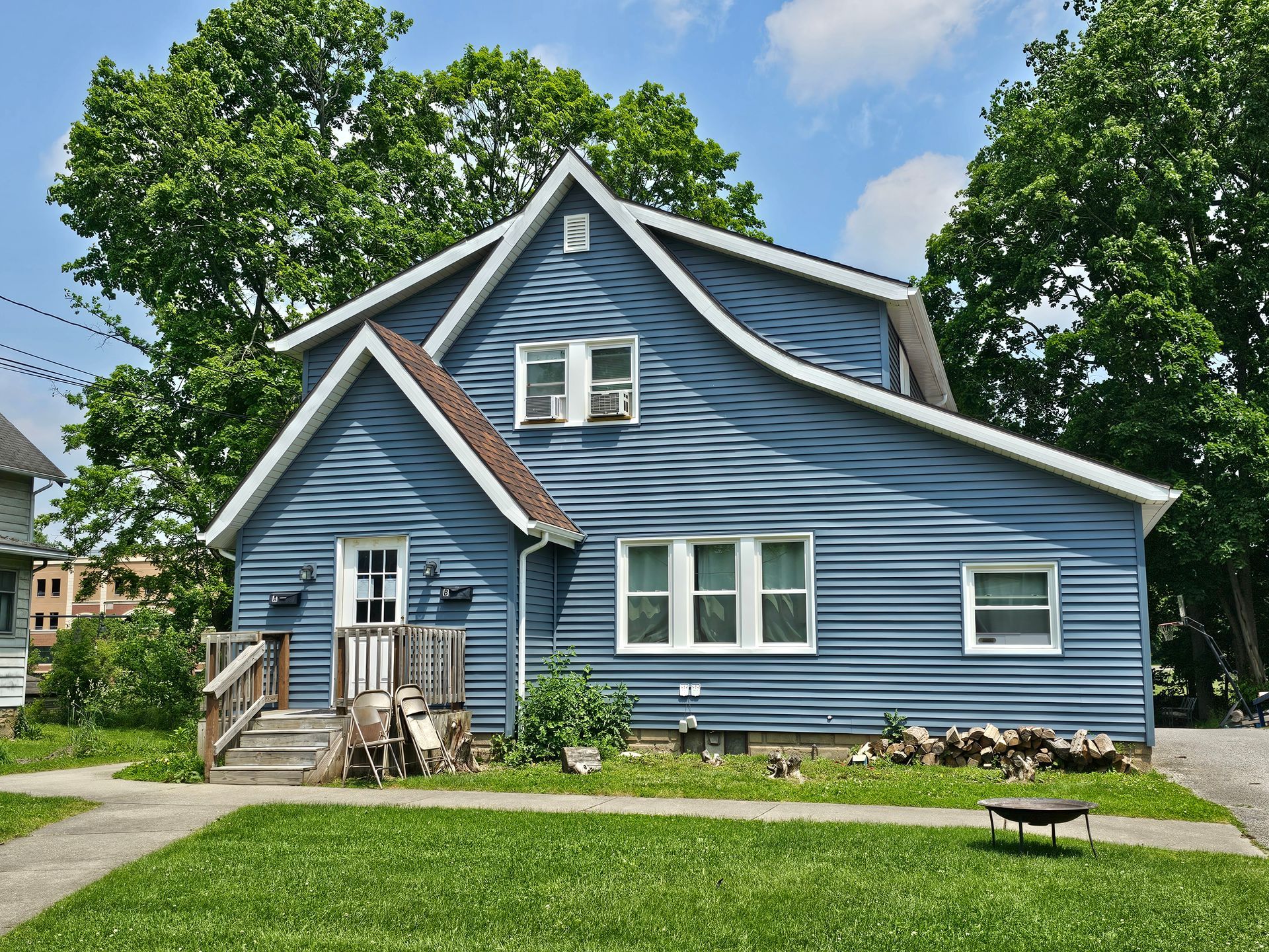 Blue two-story house with white trim, porch, and green lawn under a partly cloudy sky