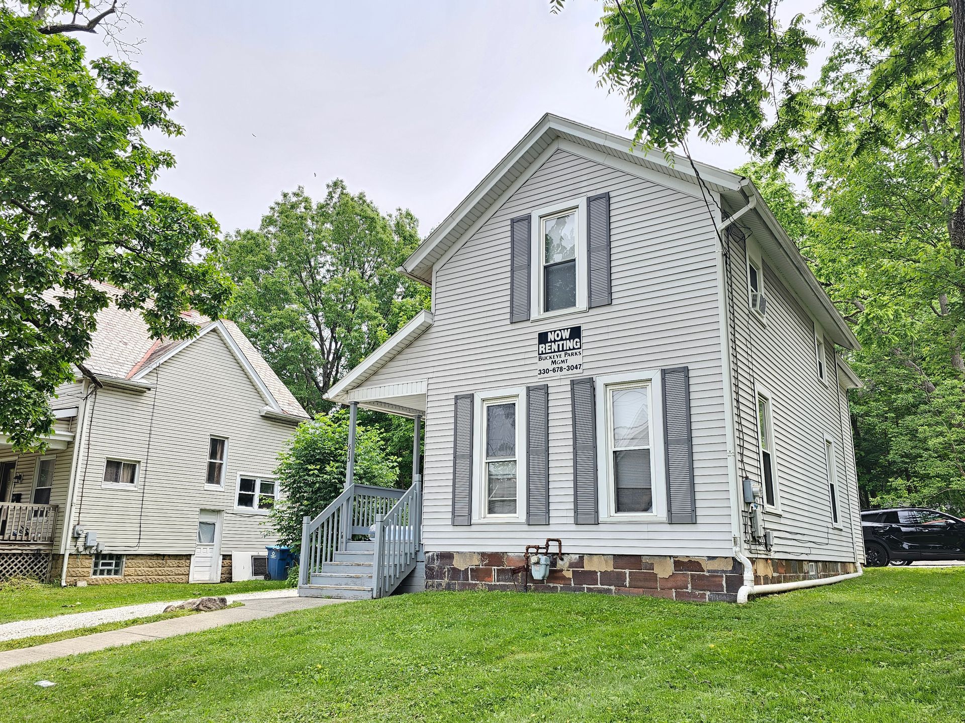 Two gray houses on a tree-lined street, with a white-and-gray home in the foreground.