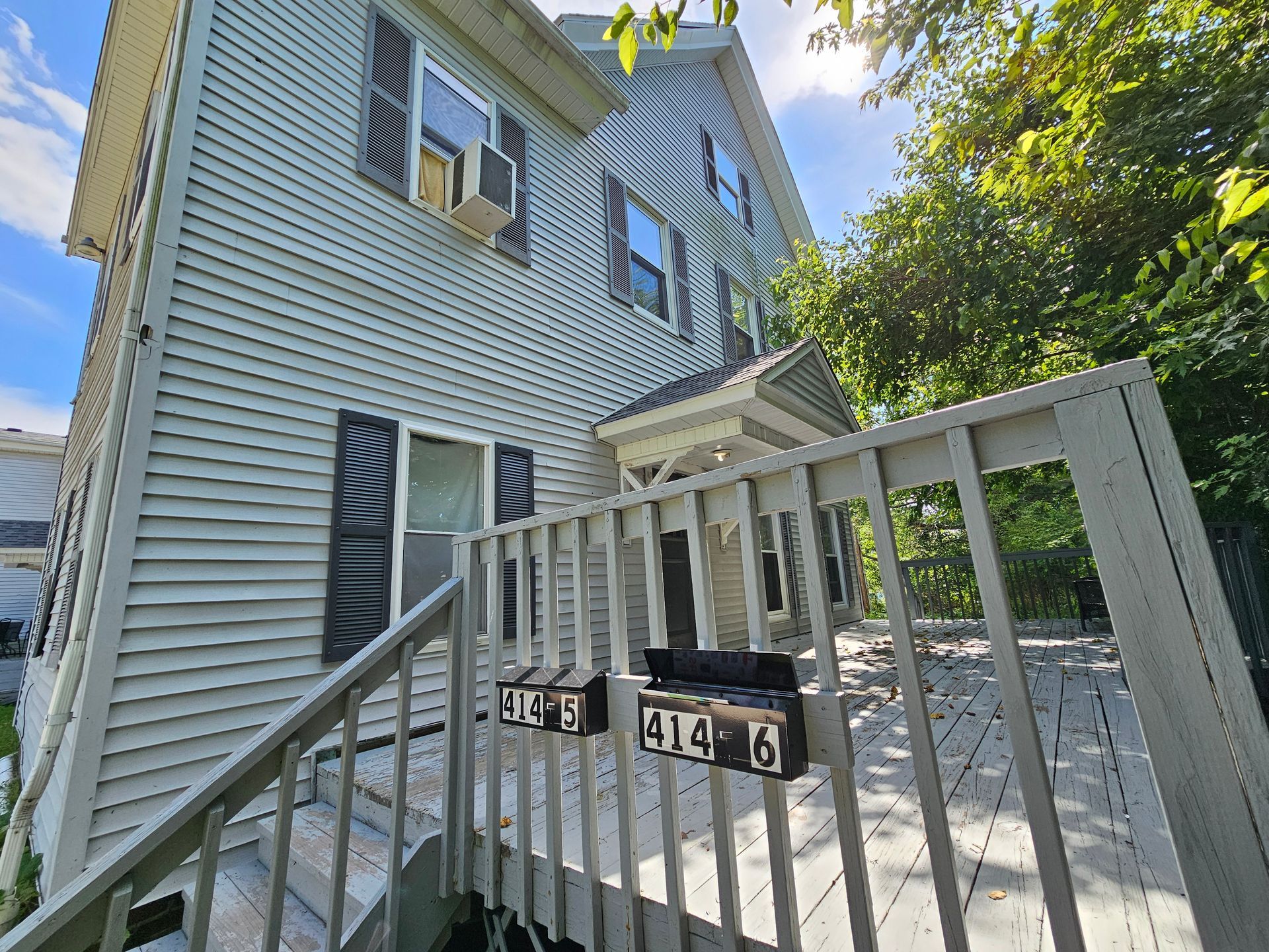 Front porch of a gray house with white railings and stairs, viewed from below in bright sunlight