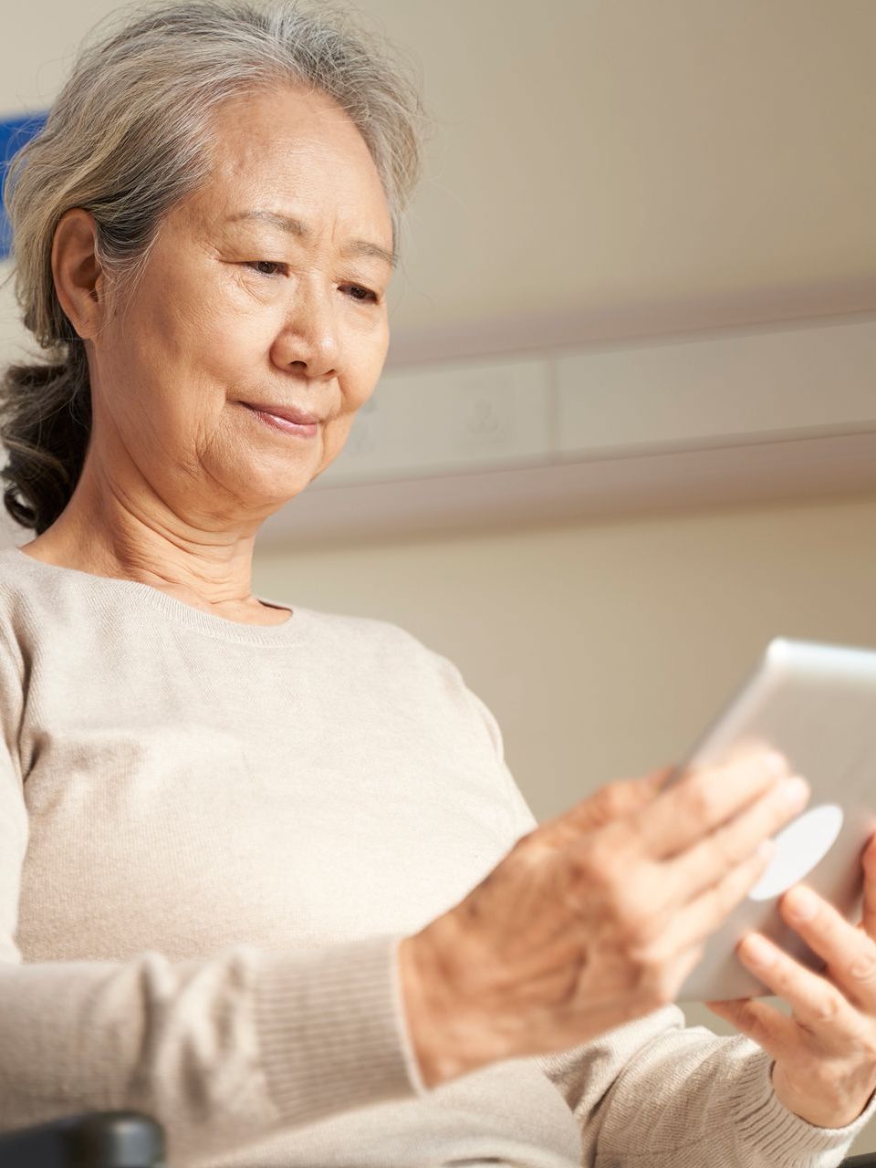 An elderly woman in a wheelchair is using a tablet computer.