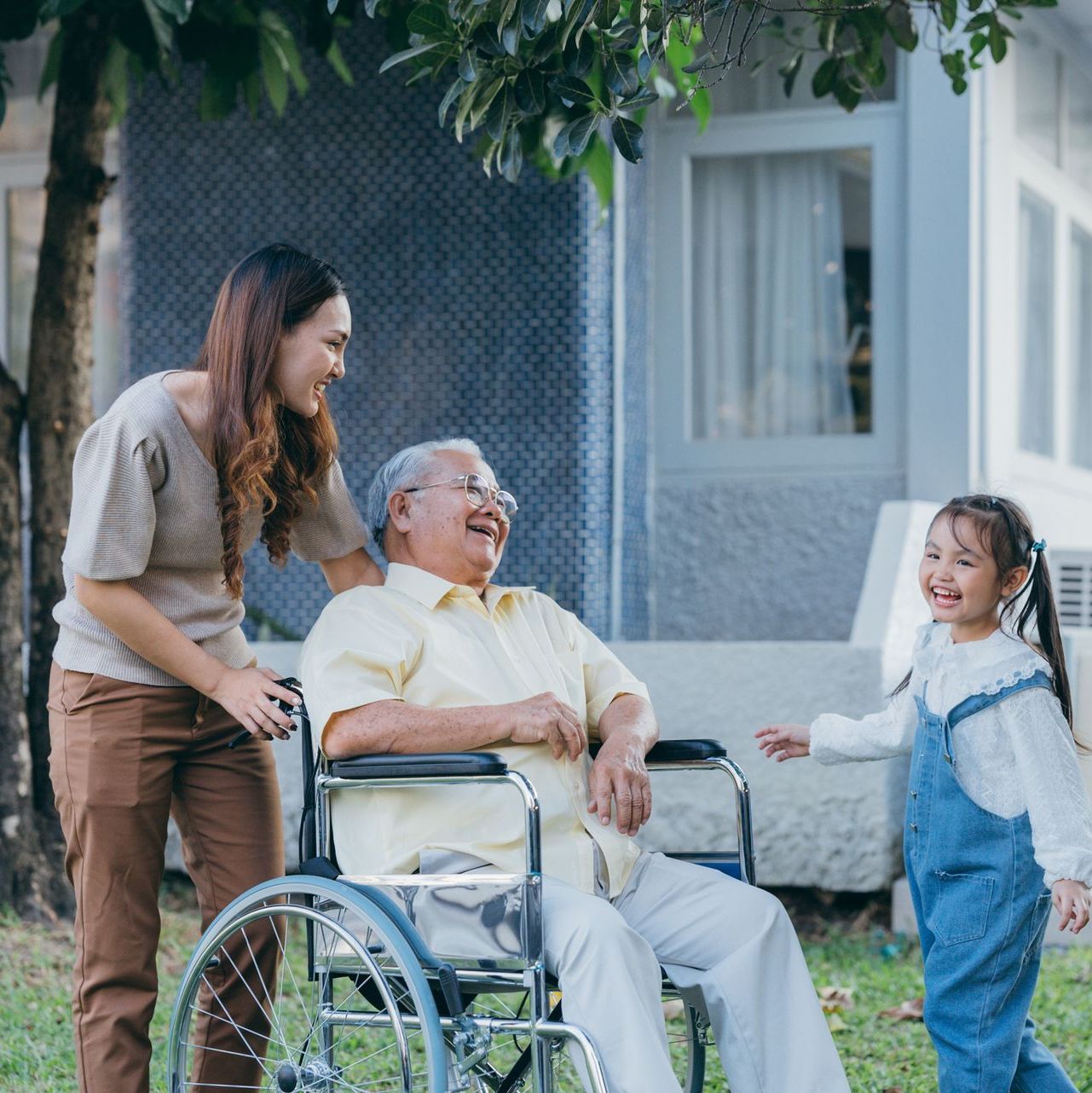 A woman and a little girl are standing next to an older man in a wheelchair.