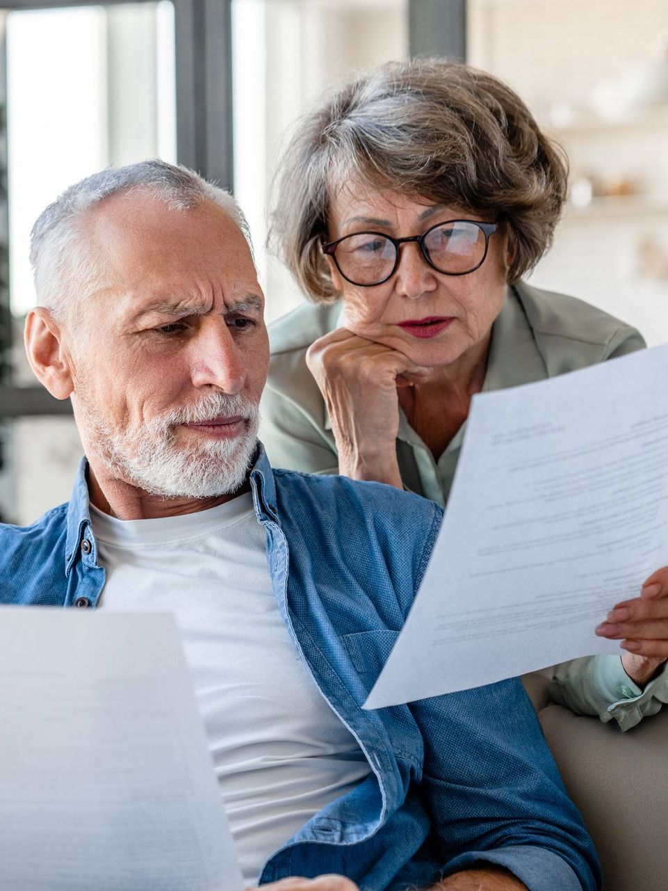 An elderly couple is sitting on a couch looking at a piece of paper.