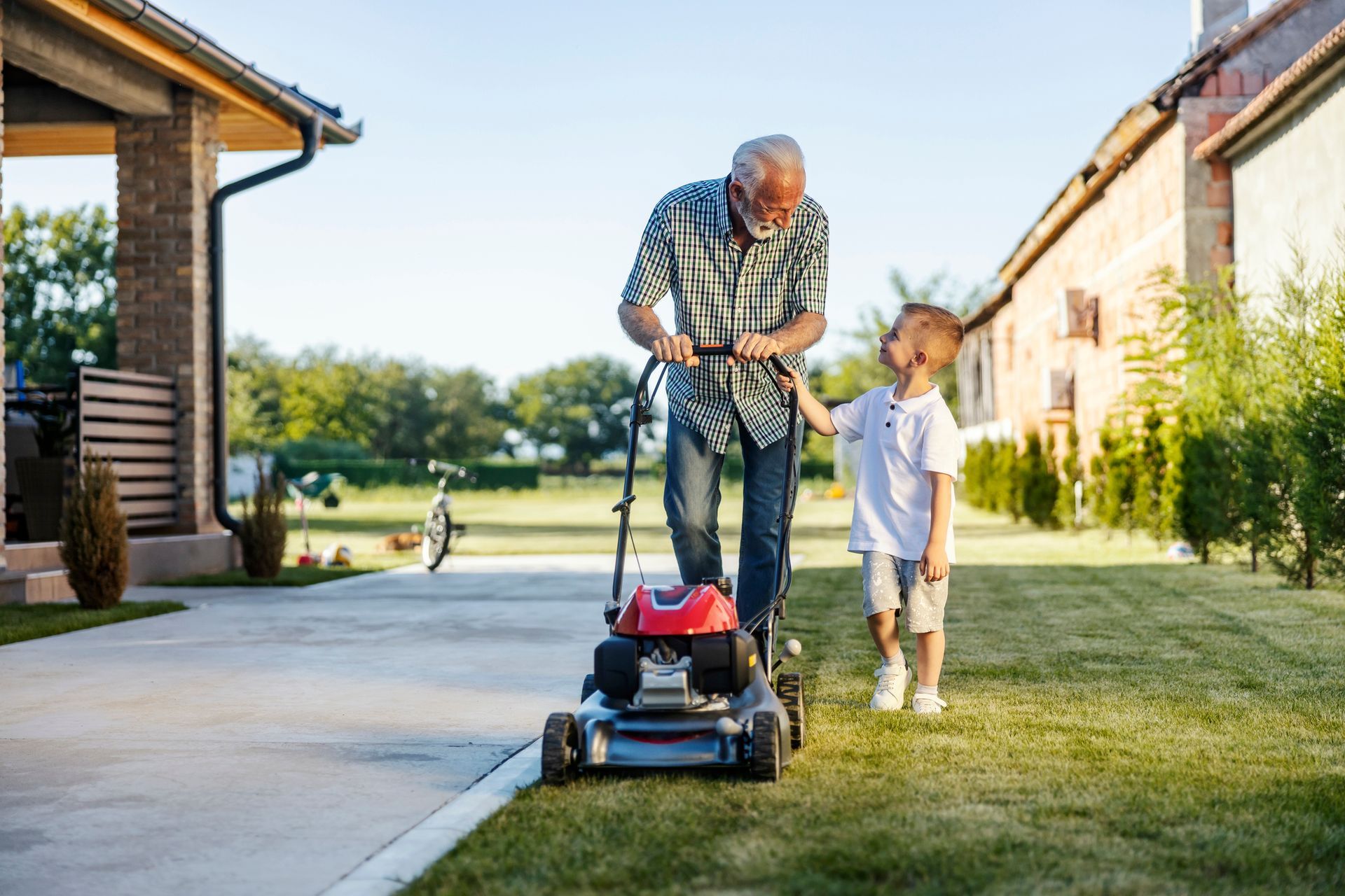 An elderly man is mowing the lawn with his grandson.