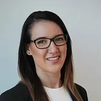 A woman wearing glasses and a black jacket is smiling for the camera.