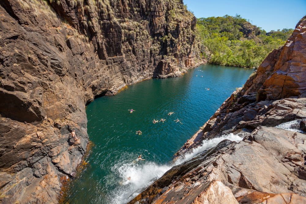 People Swimming and Cliff Diving in a Natural Rock Pool Surrounded by Steep Cliffs — NT Driver Guide - Escorted Touring & Transfers in Darwin City, NT