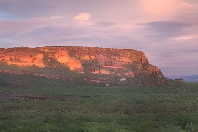 Sunset Illuminates a Rugged Cliff Rising Above Green Field — NT Driver Guide - Escorted Touring & Transfers in Darwin City, NT