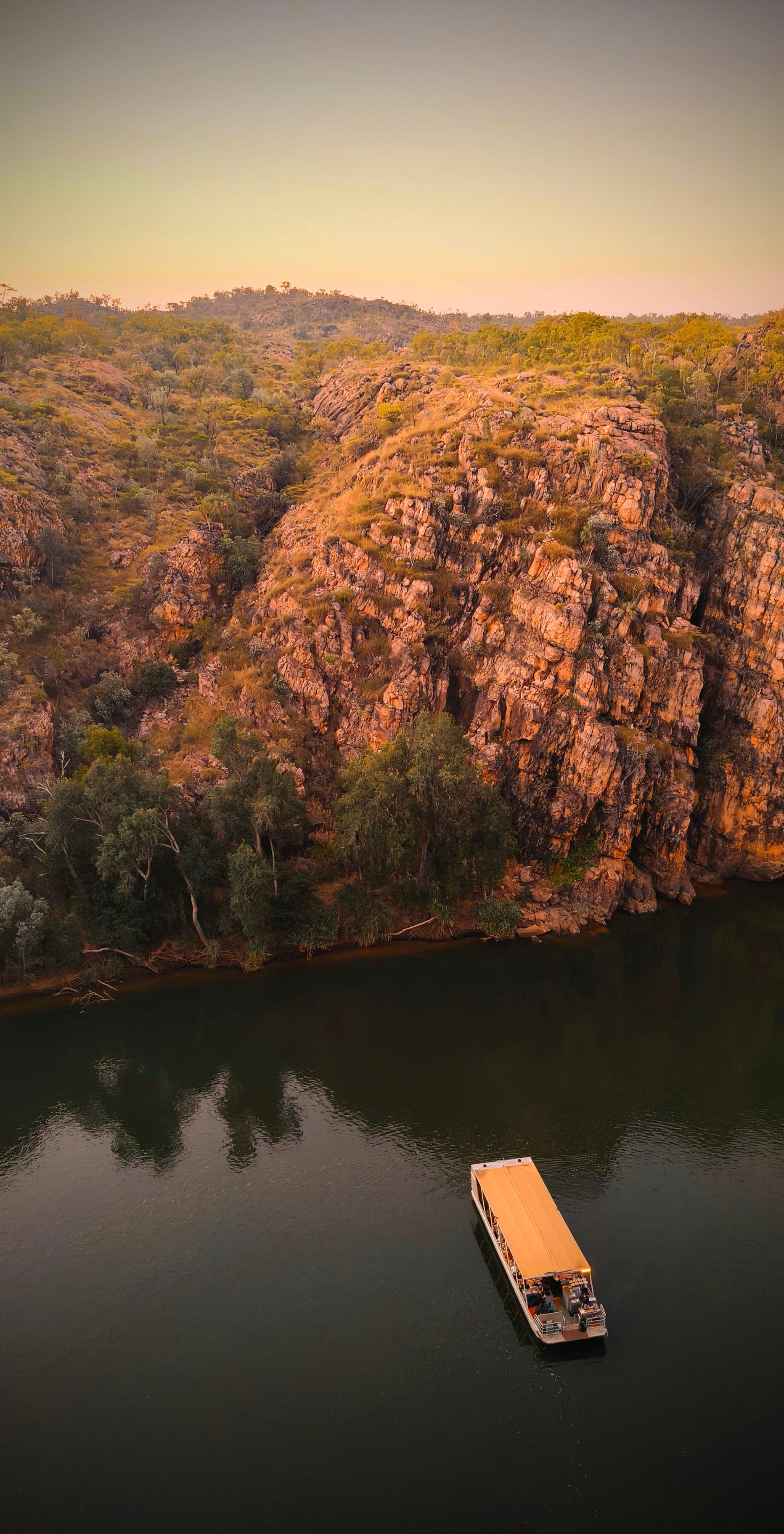 Boat on water near a rocky hillside with trees. Sunset hues — NT Driver Guide - Escorted Tours & Transfers in Darwin City, NT
