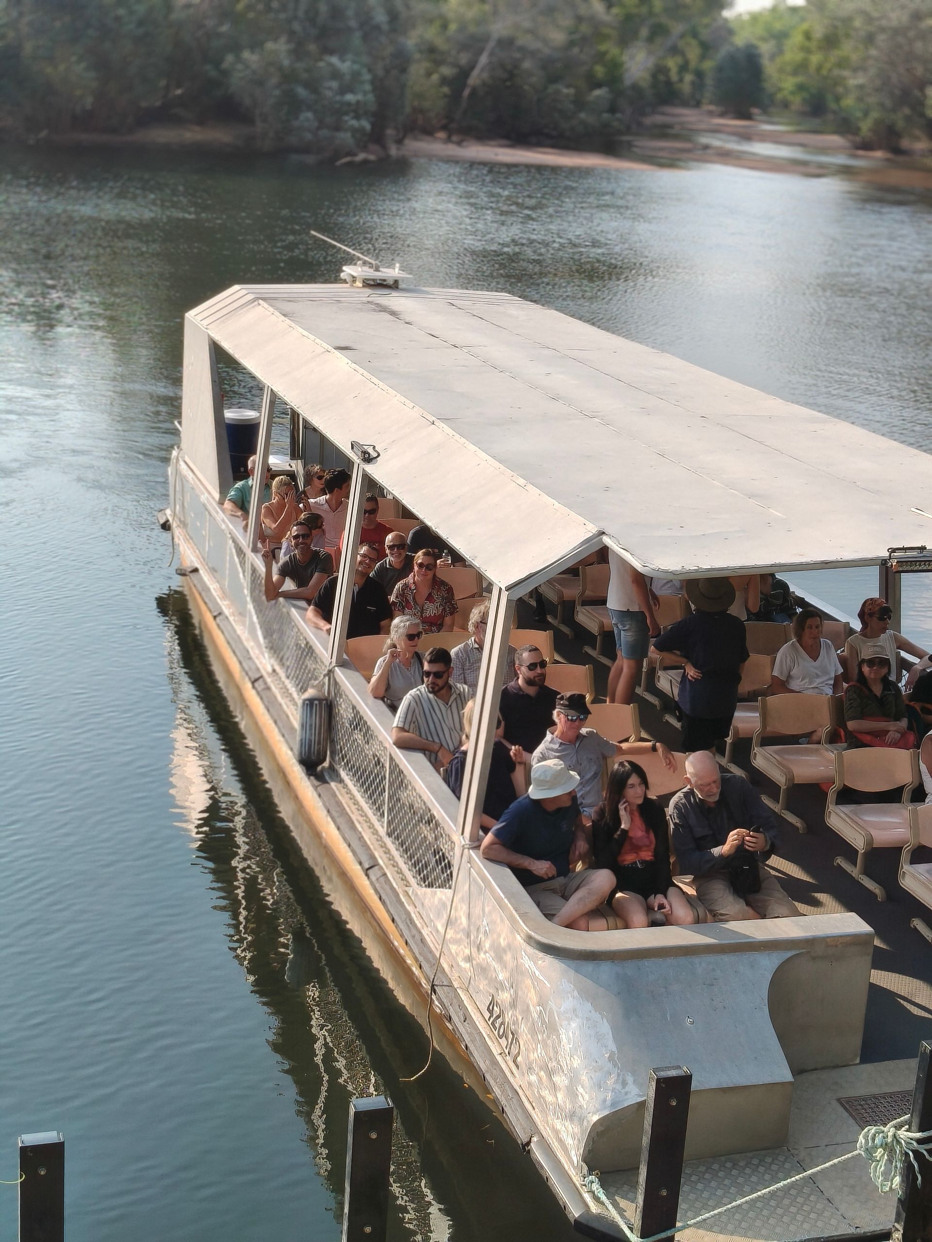 Boat filled with passengers on a river. Grey boat with white roof, people seated, scenic background - Escorted Tours & Transfers in Darwin City, NT
