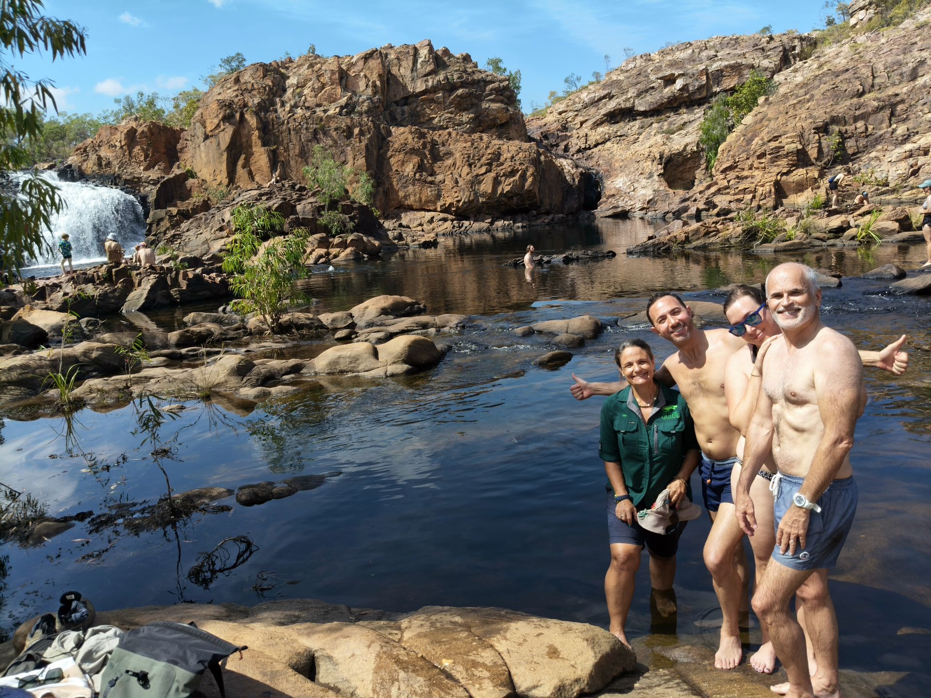 People swimming near waterfall and rocky landscape. Sunny, clear sky — NT Driver Guide - Escorted Tours & Transfers in Darwin City, NT