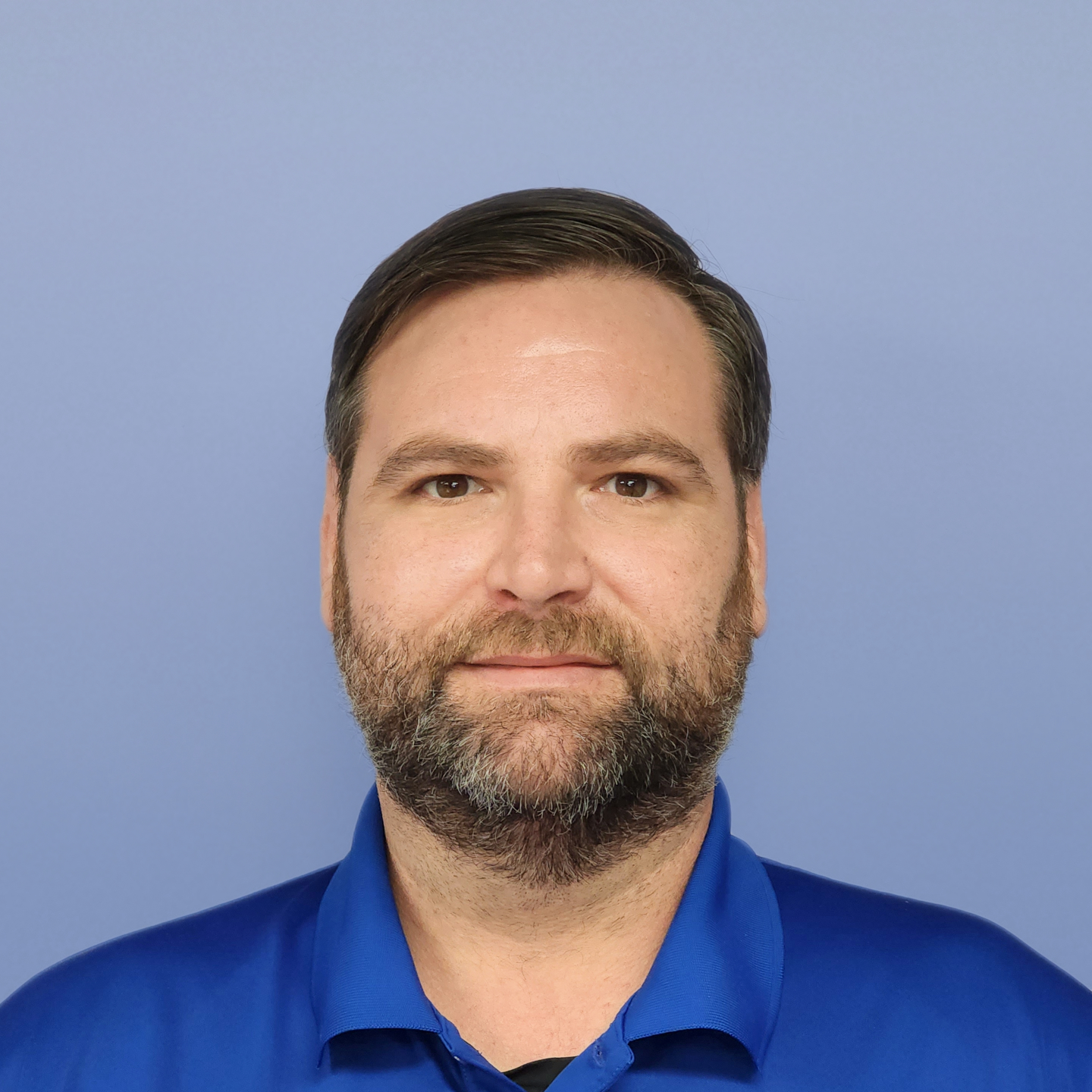 Man with a beard in a blue shirt smiling, against a blue backdrop.