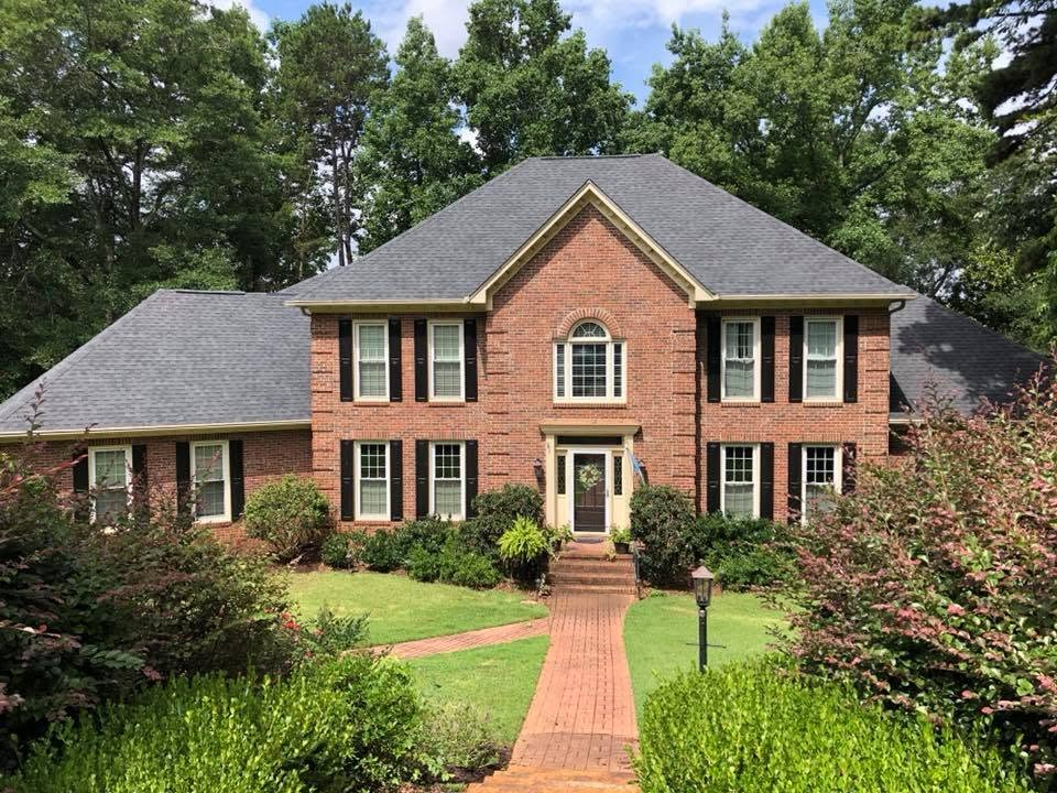Single-story brick house with a porch, green lawn, and driveway under a partly cloudy sky