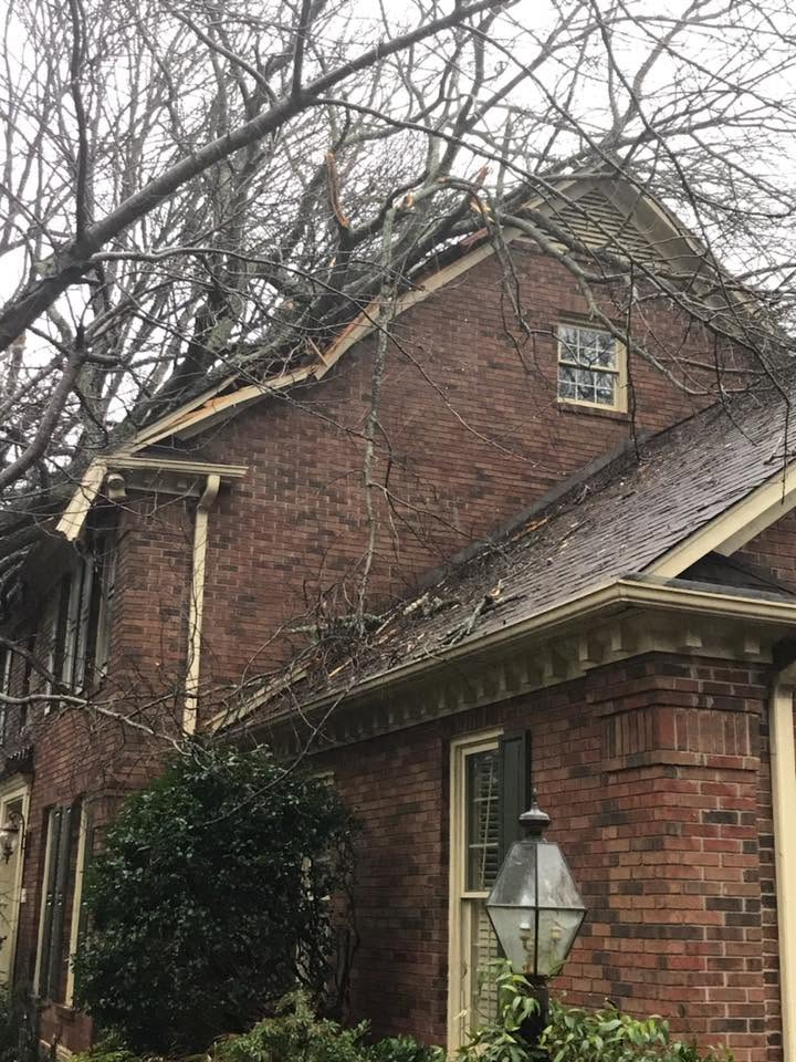 Large white two-story house with a wraparound porch, parked vehicles, and bare trees on a cloudy day