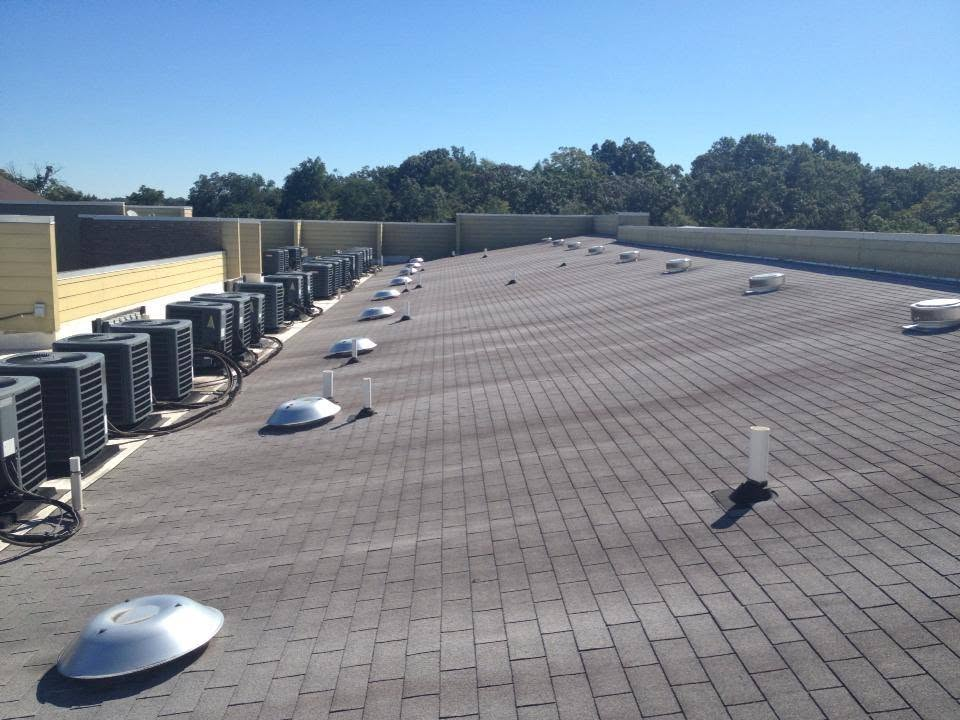 House roof under construction with exposed plywood, parked cars in front, and a clear blue sky.