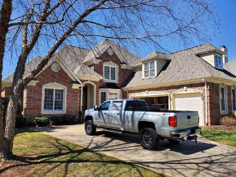 Silver pickup truck parked in driveway of a brick suburban house on a sunny day