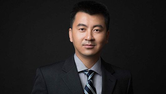 一位穿着西装打着领带的男人站在黑色背景前。