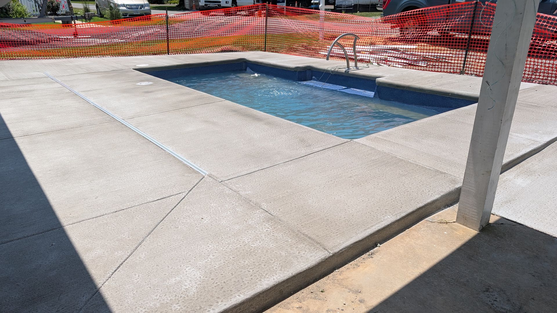 A small rectangular swimming pool surrounded by a new, light-gray concrete patio under construction.
