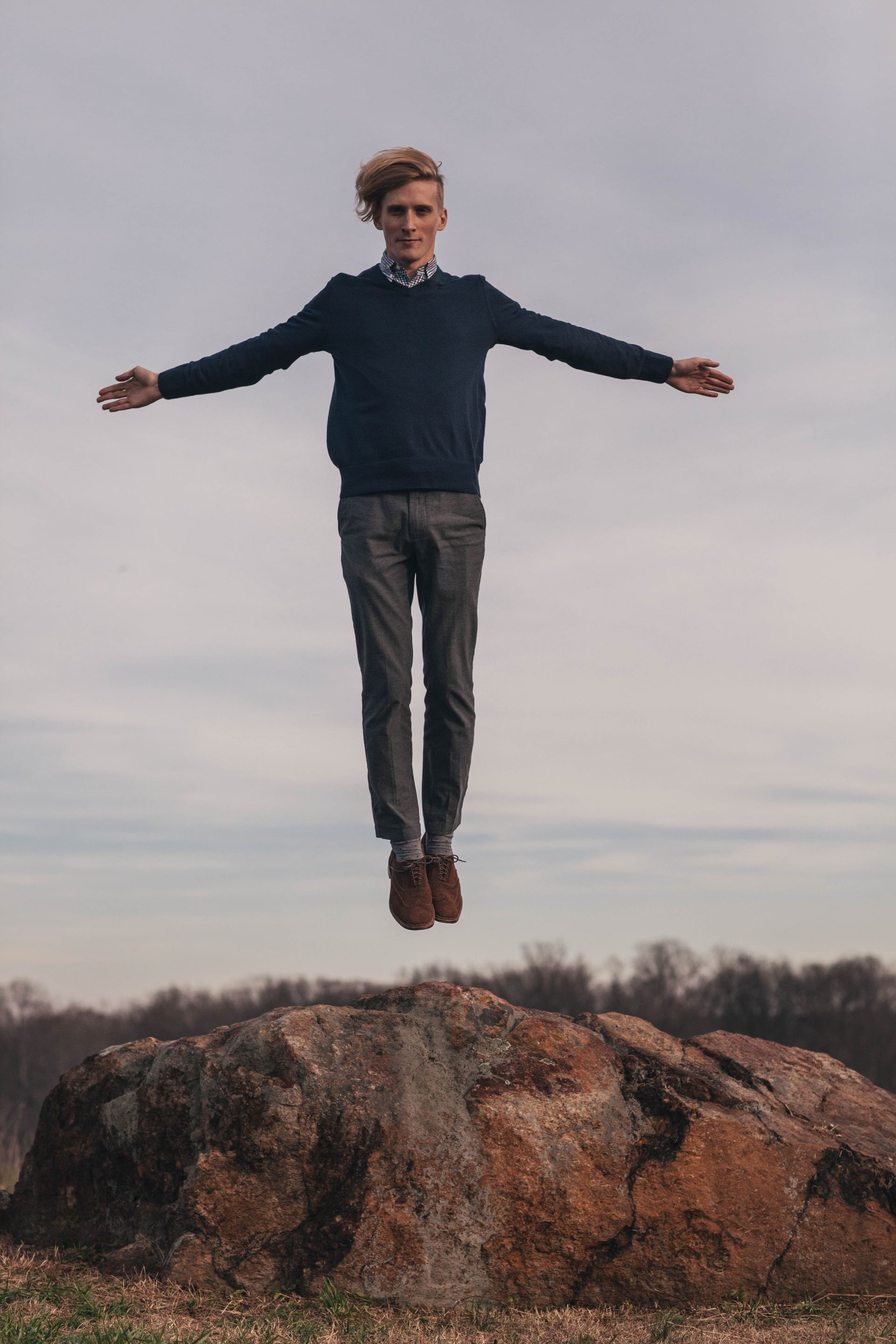 A man is jumping in the air over a rock.