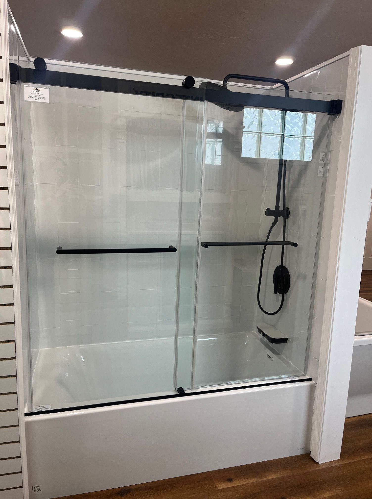 Glass shower enclosure with a black handrail and overhead shower fixture in a tiled bathroom.