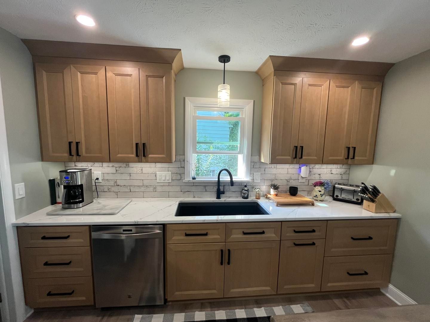 Modern kitchen with wood cabinets, white countertops, stainless appliances, and a window over the sink.