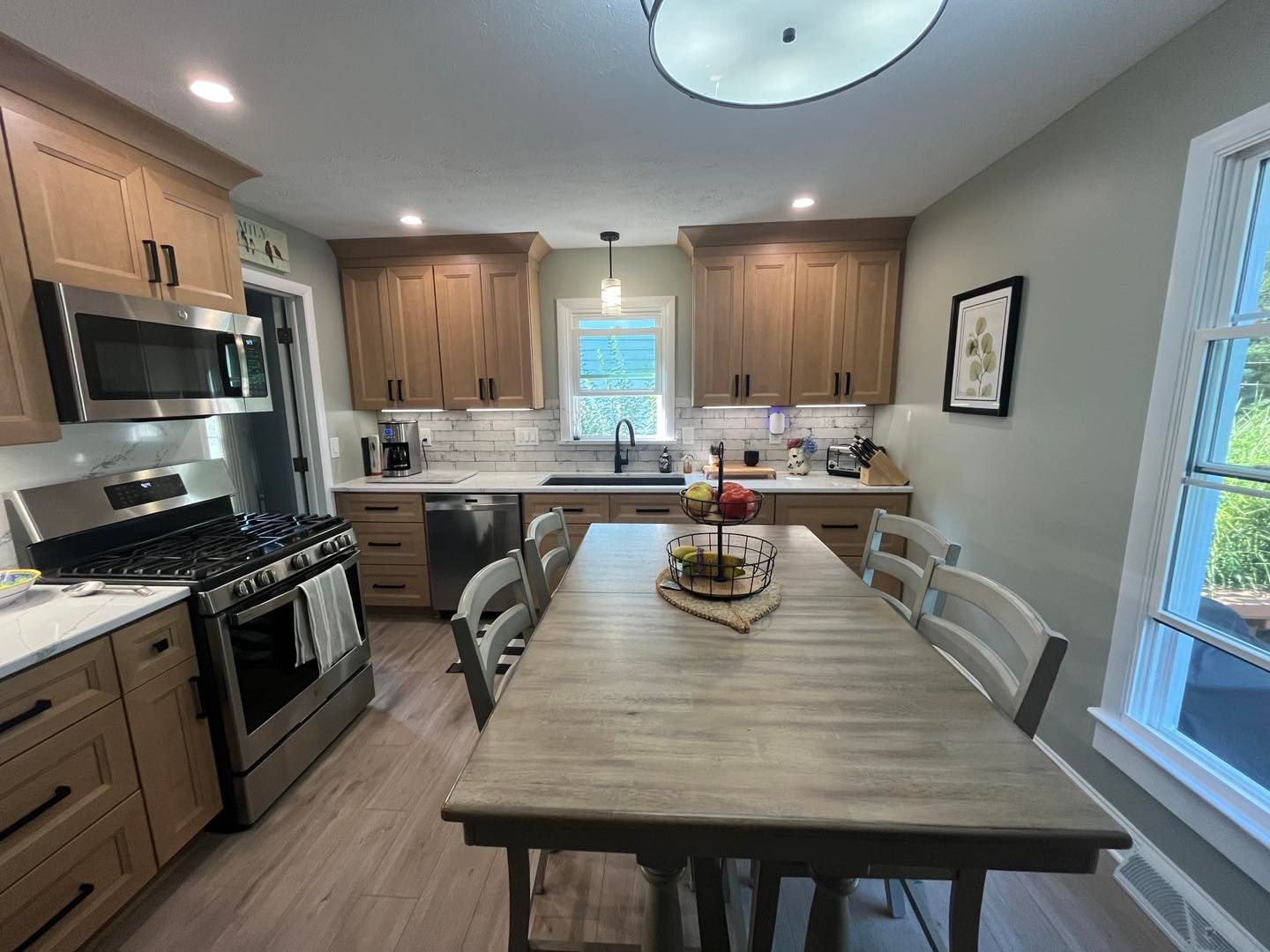 Bright kitchen with wood cabinets, stainless stove, central dining table, and windows.