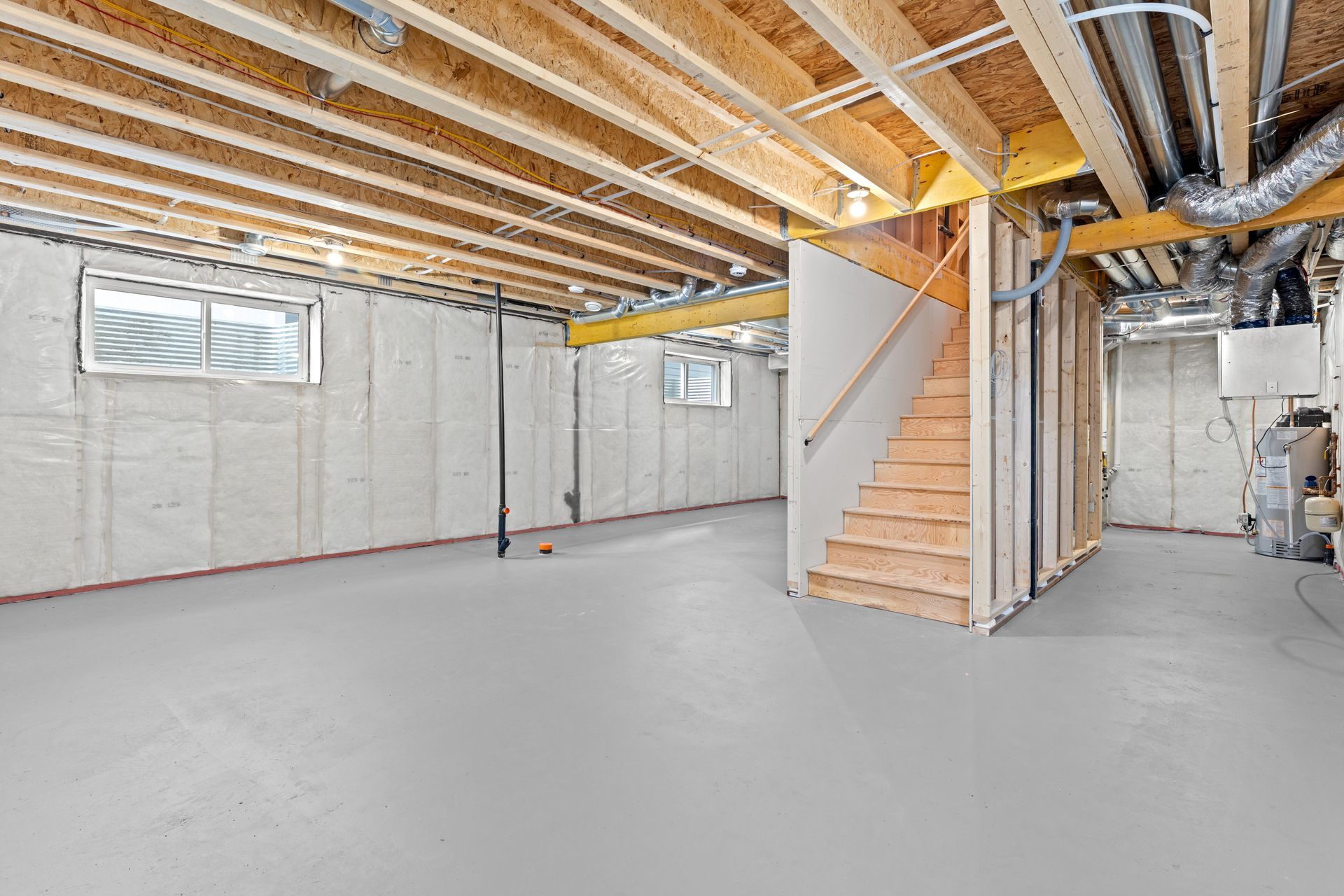 Unfinished basement with exposed beams, concrete floor, windows, stairs, and utility equipment.