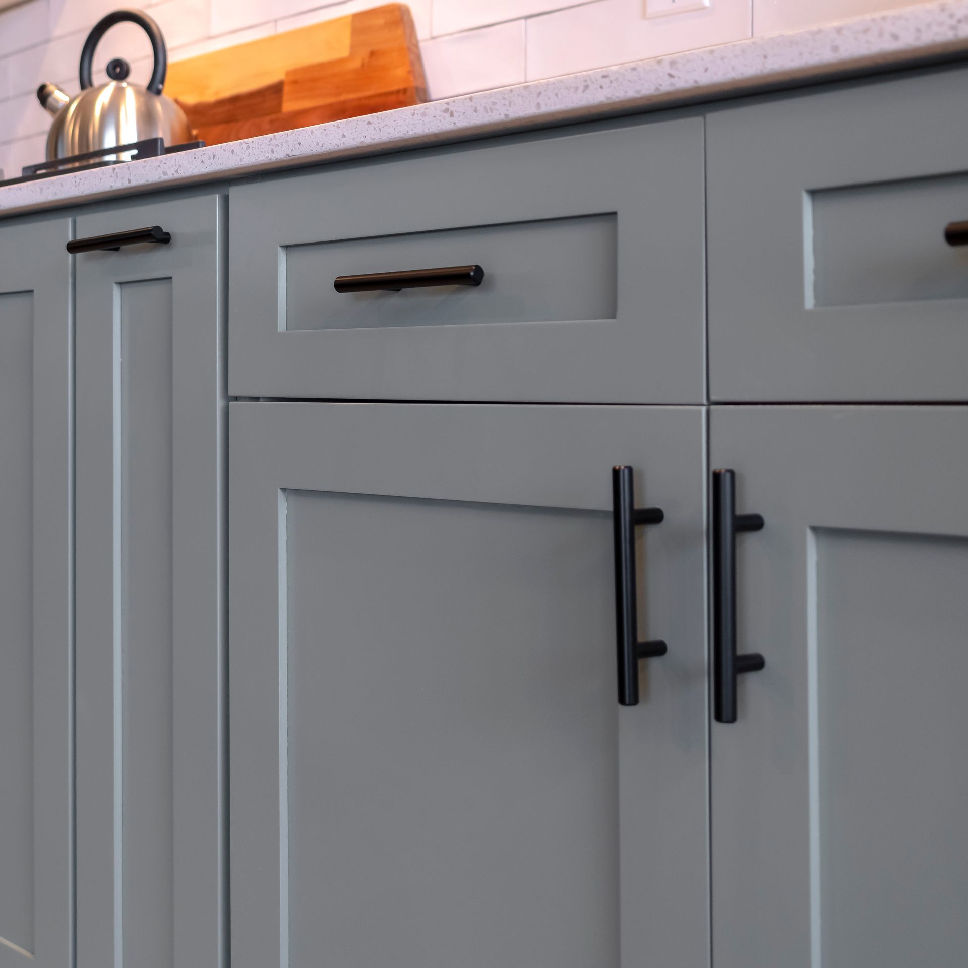 Gray kitchen cabinets with black handles beneath a countertop and kettle.