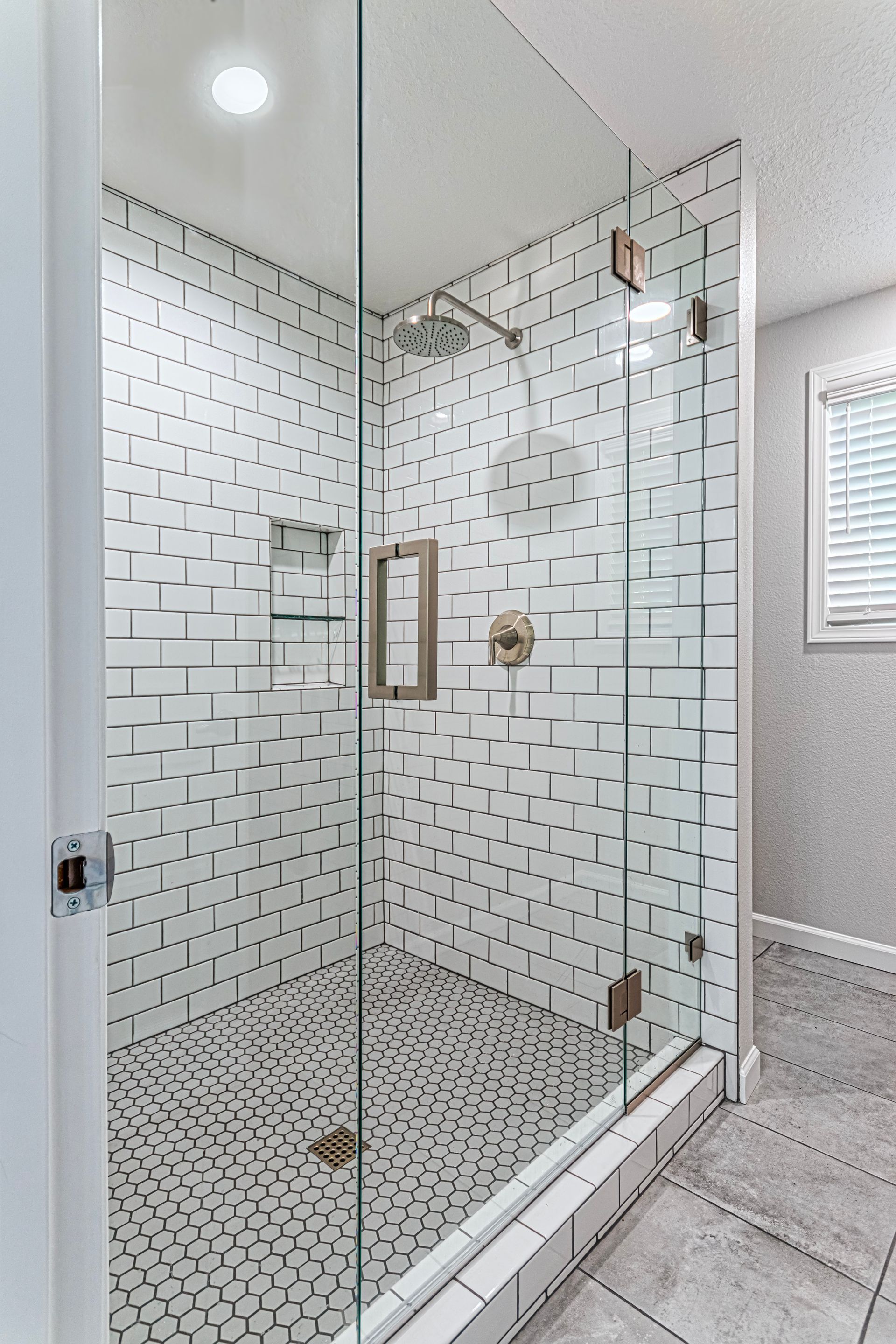 Glass shower enclosure with white subway and mosaic tile in a bright bathroom.