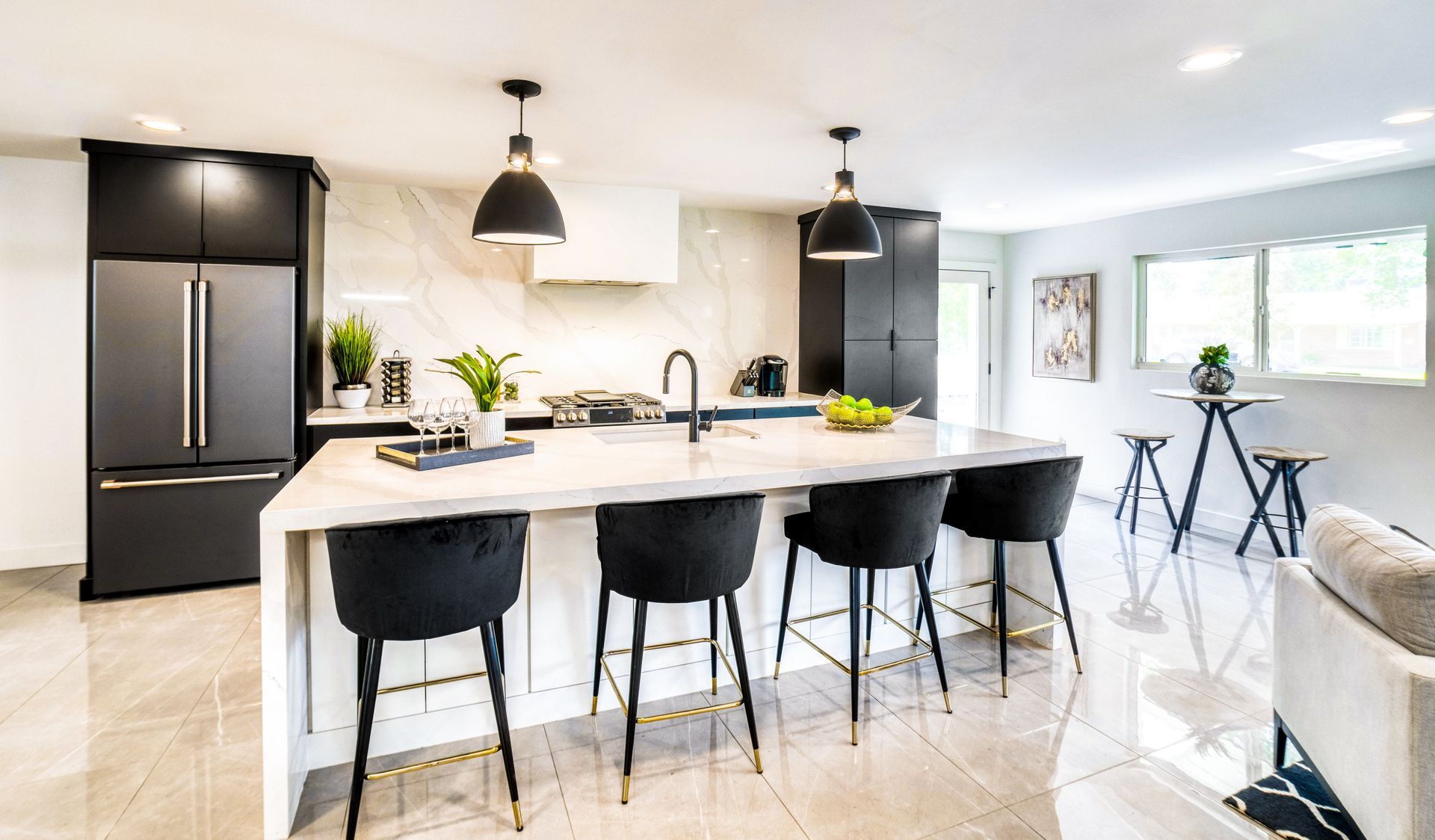 Modern bright kitchen with black island, pendant lights, and bar stools in an open living space.