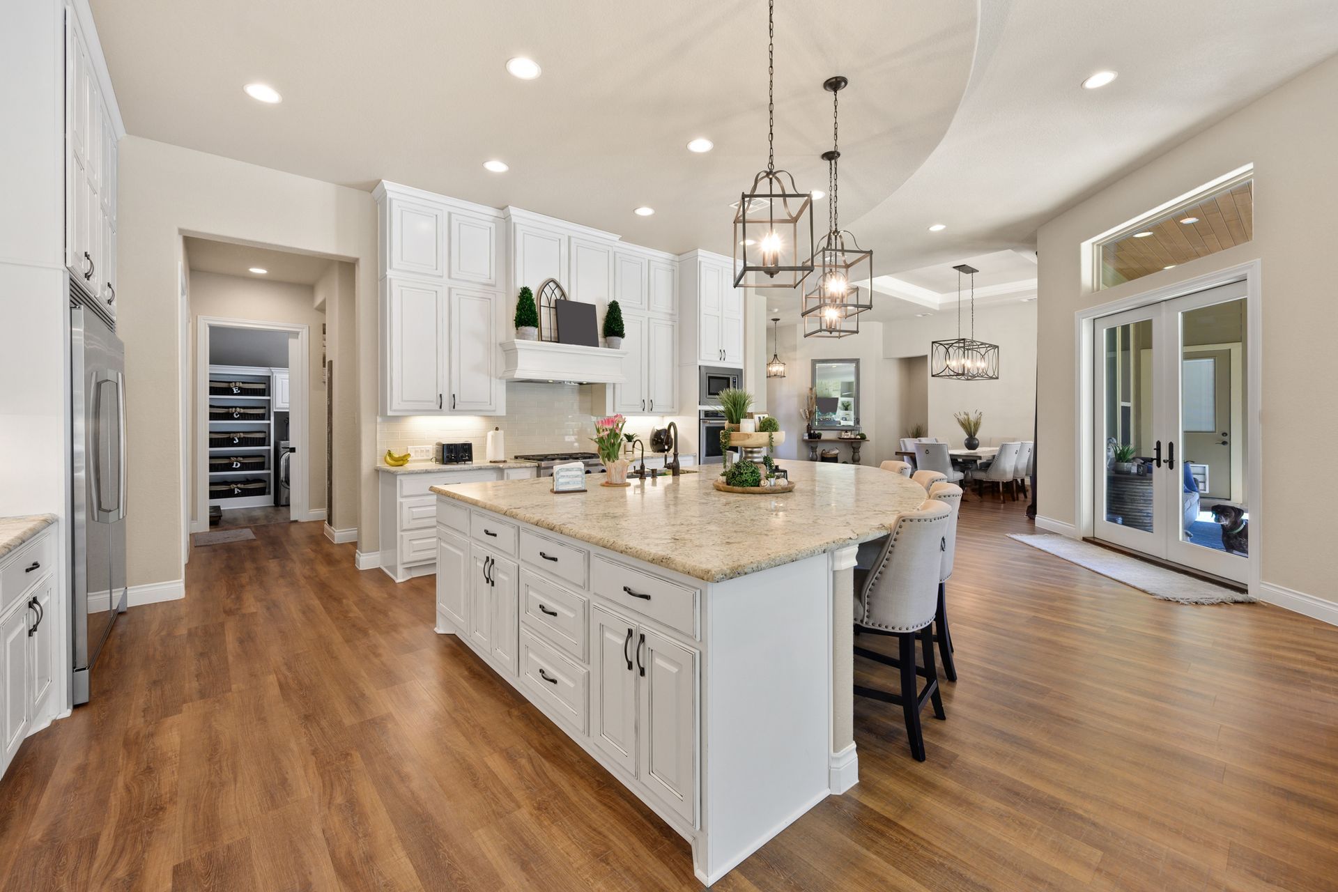 Bright modern kitchen with white cabinets, large island, and wood floors, open to a sunlit living area.