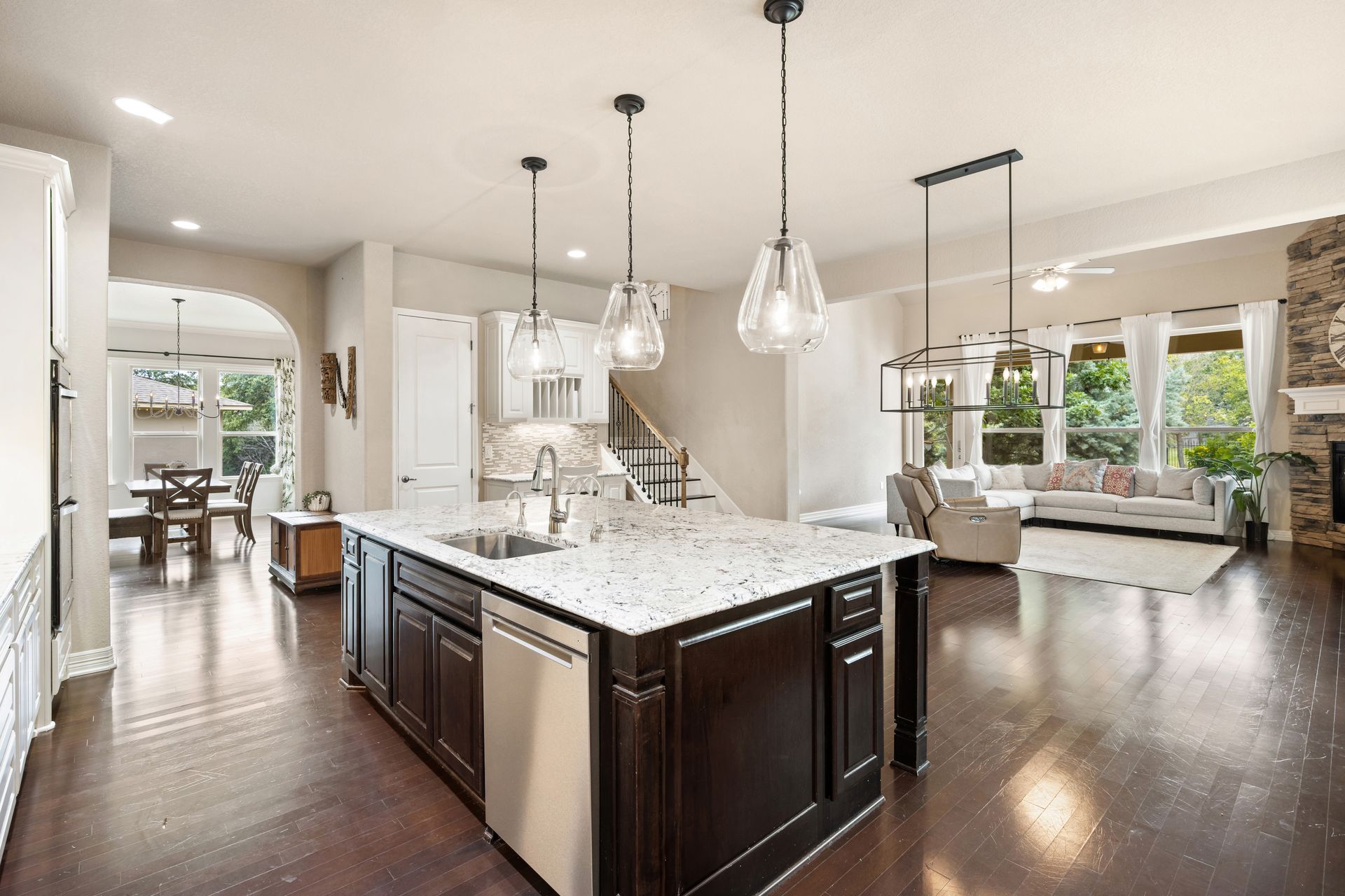 Spacious modern kitchen and living area with a large island, dark floors, and pendant lights.