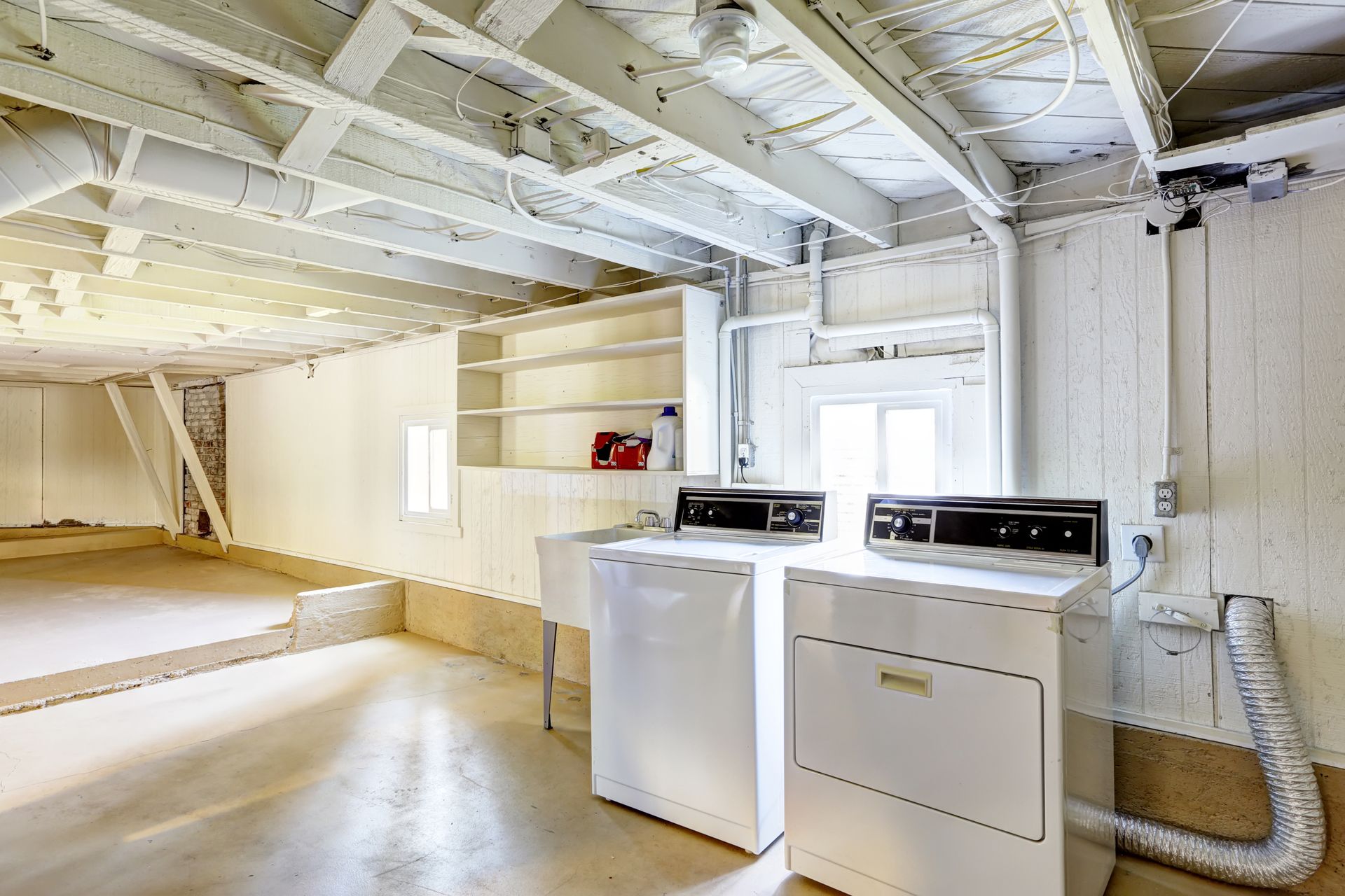 Laundry area in unfinished basement with white washer, dryer, and exposed beams.