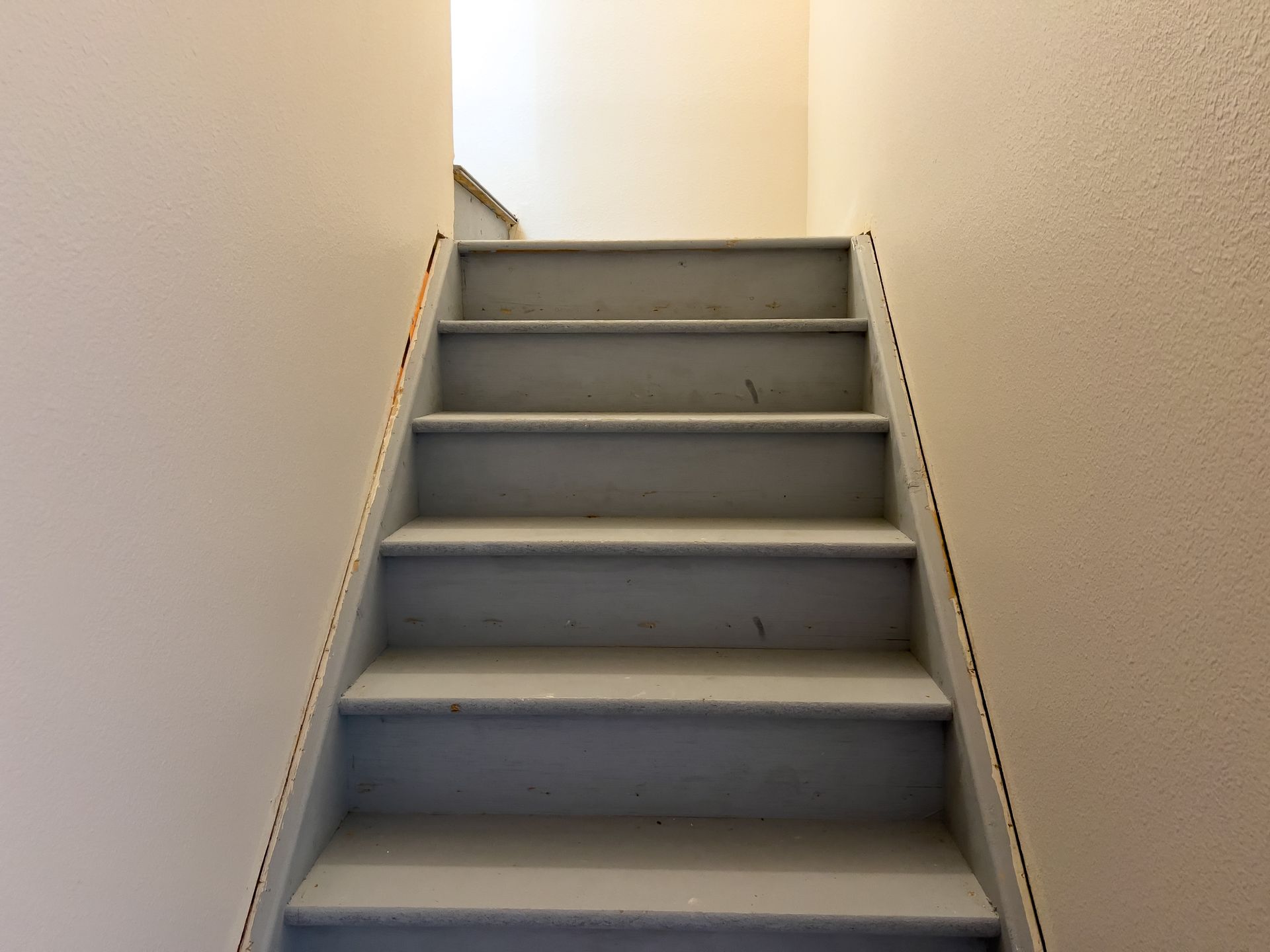 Narrow indoor staircase with gray steps and white walls, viewed from the bottom up.