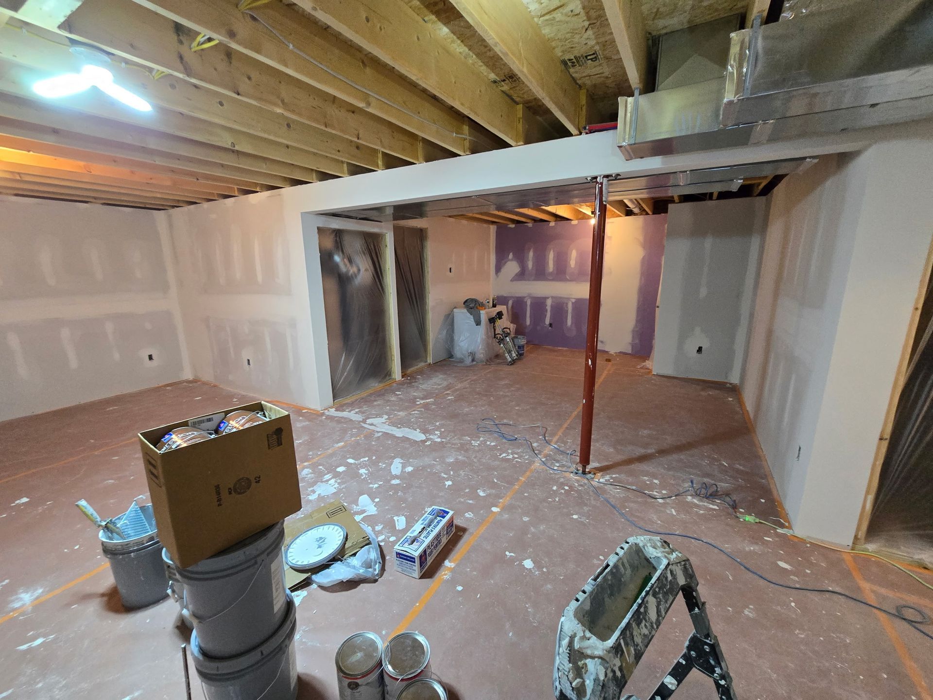 A basement under construction with a ladder and buckets of paint.
