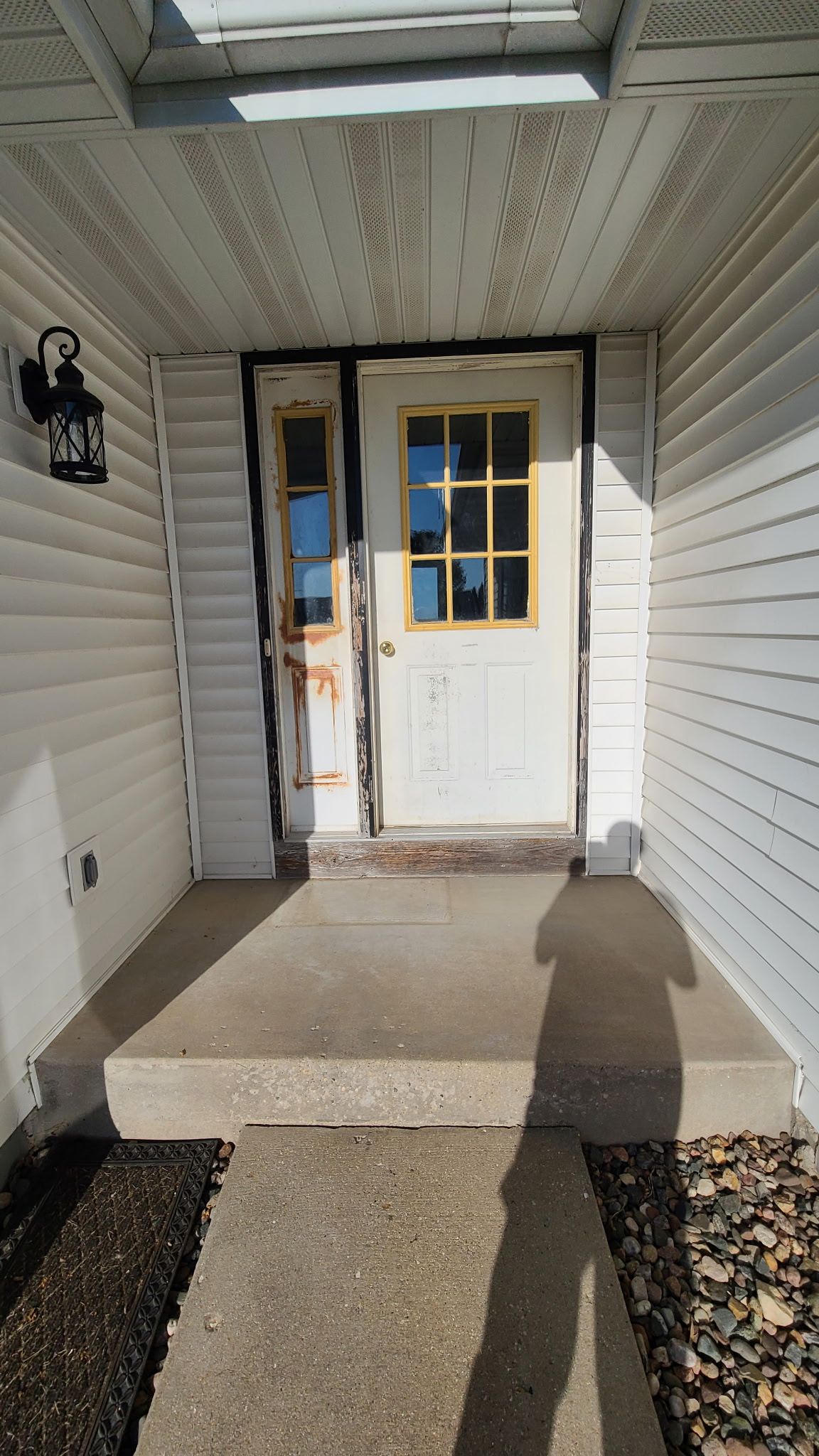 A shadow of a person is cast on the sidewalk in front of a white door.