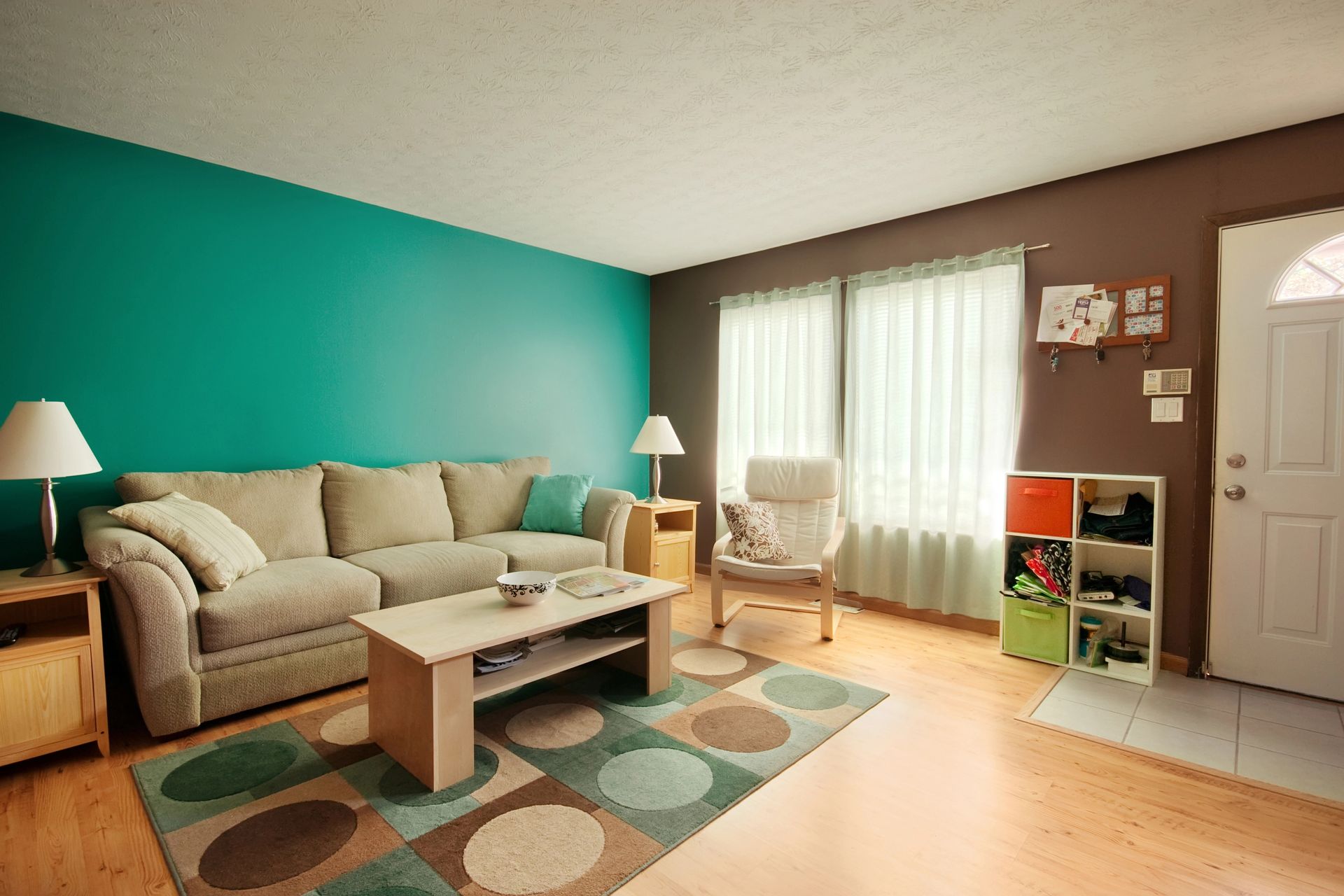 Living room with teal and brown walls, beige sofa, colorful rug, and wooden floors.