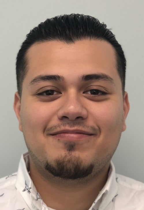 Portrait of a smiling person with short dark hair and a goatee, wearing a white collared shirt.